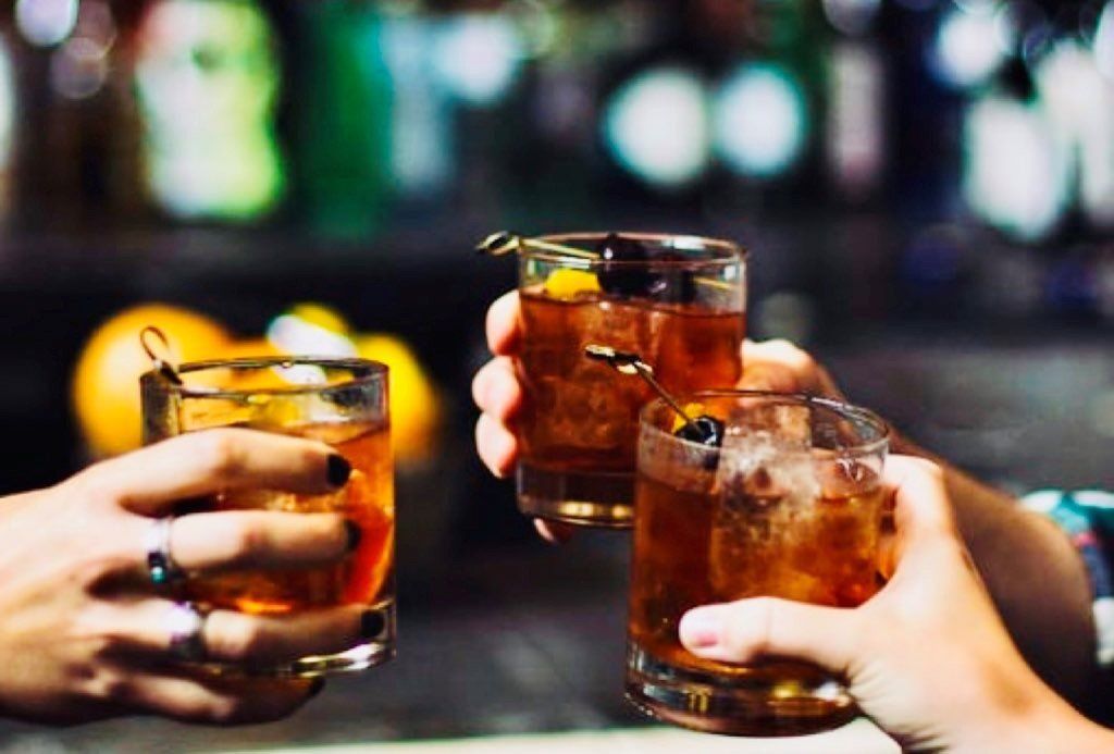 A group of people are toasting with three glasses of whiskey.