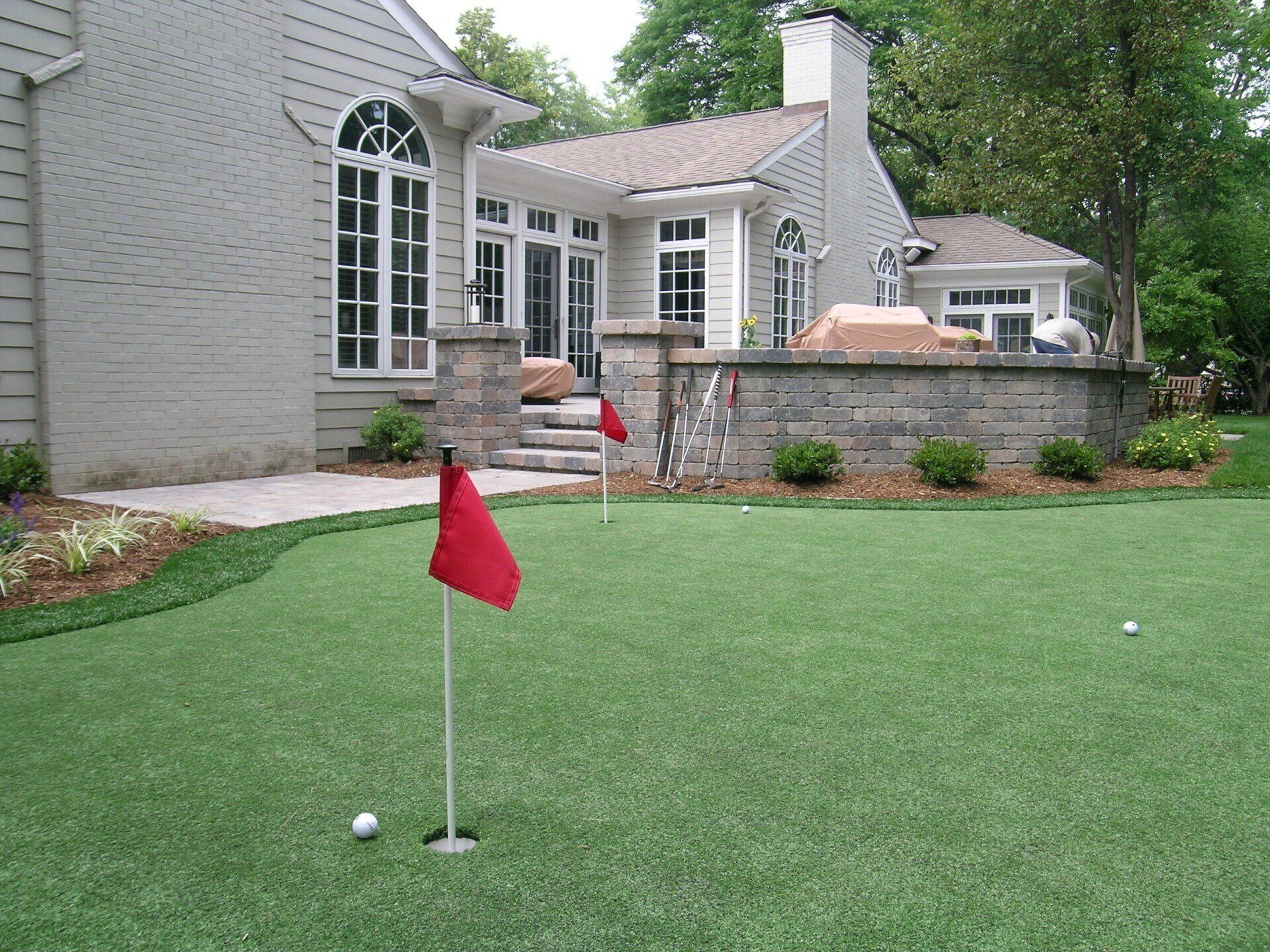 A putting green with a red flag in front of a house