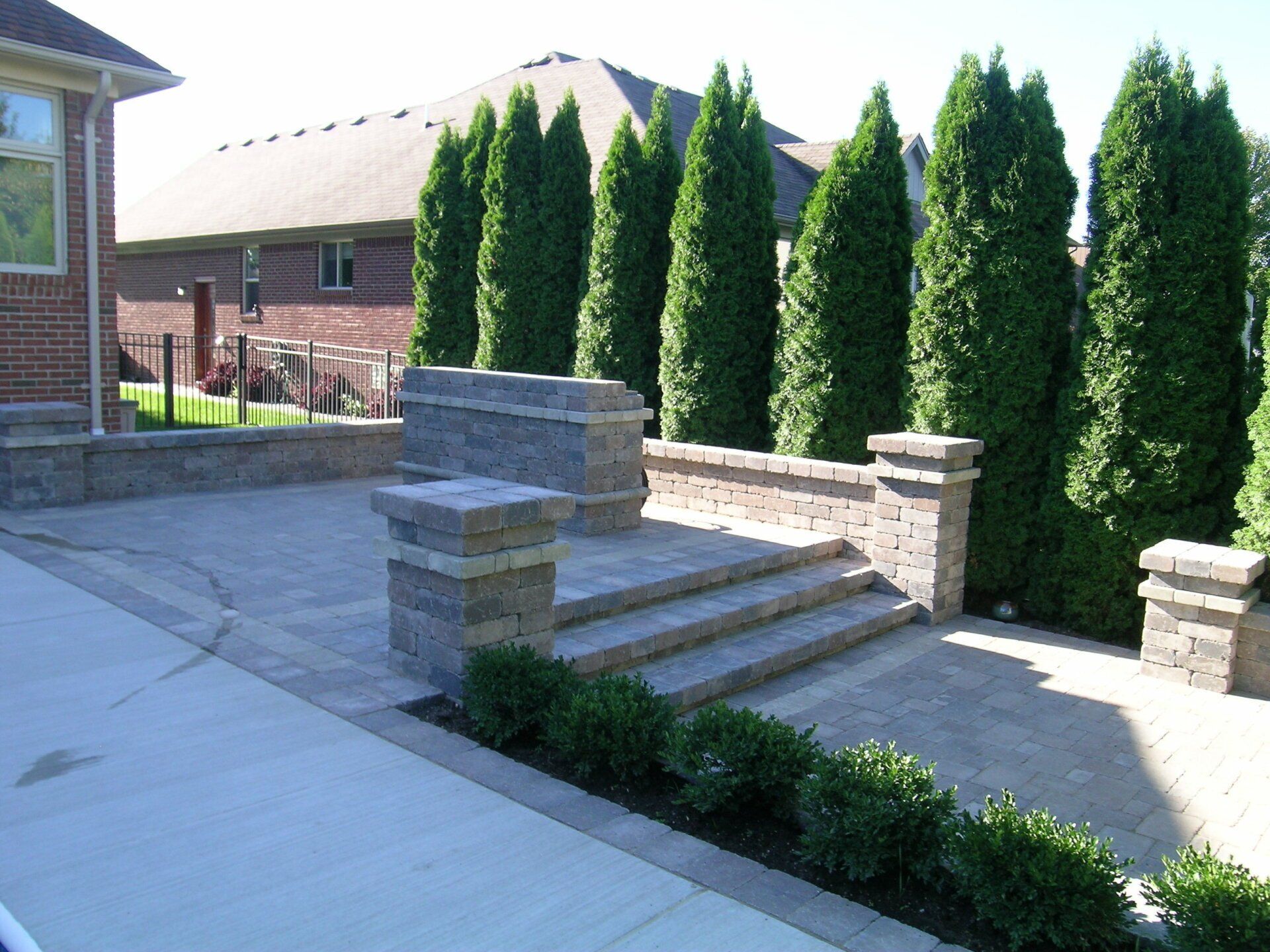 A brick patio with steps and trees in front of a brick house