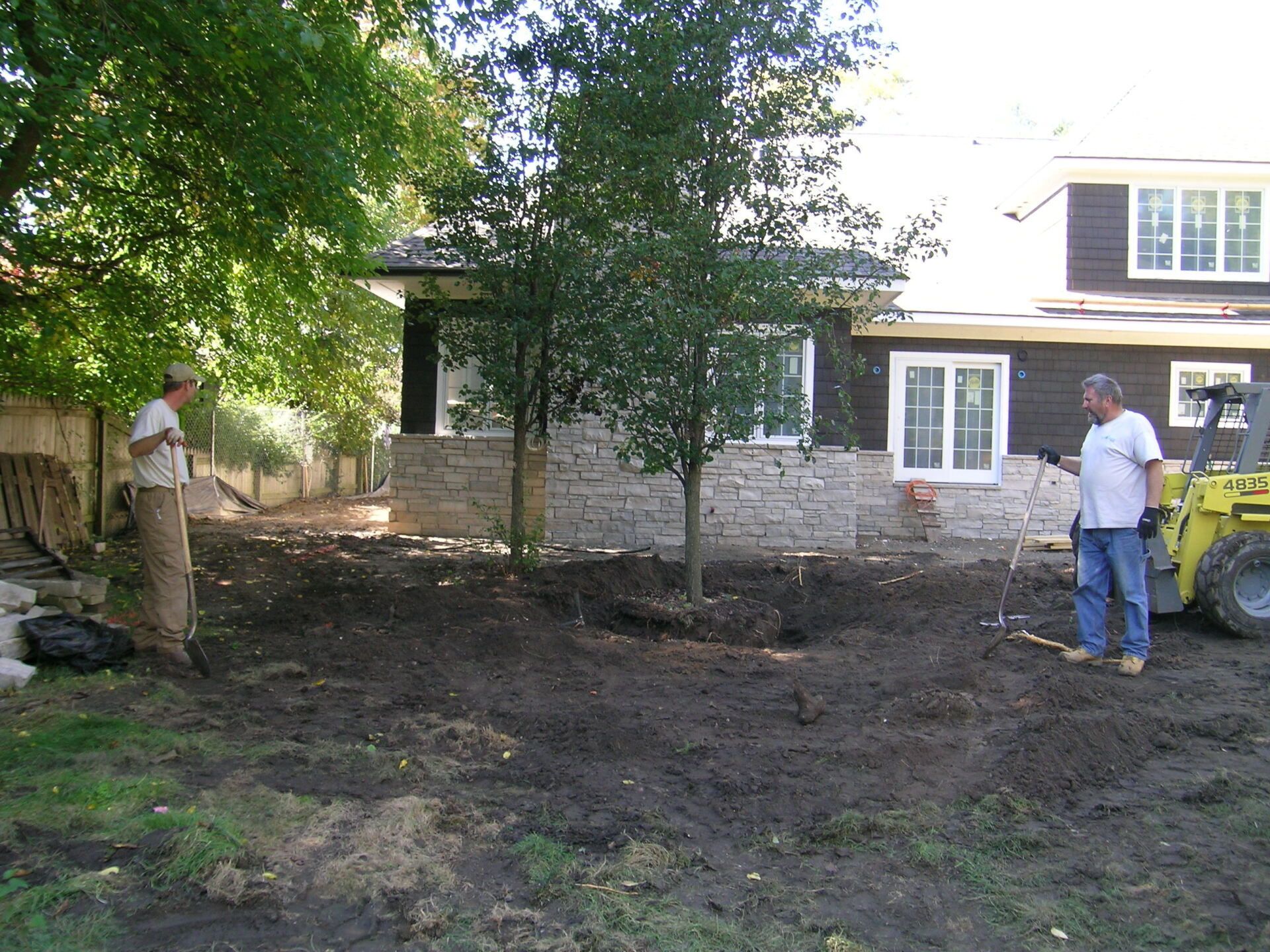 Two men are working in a yard in front of a house