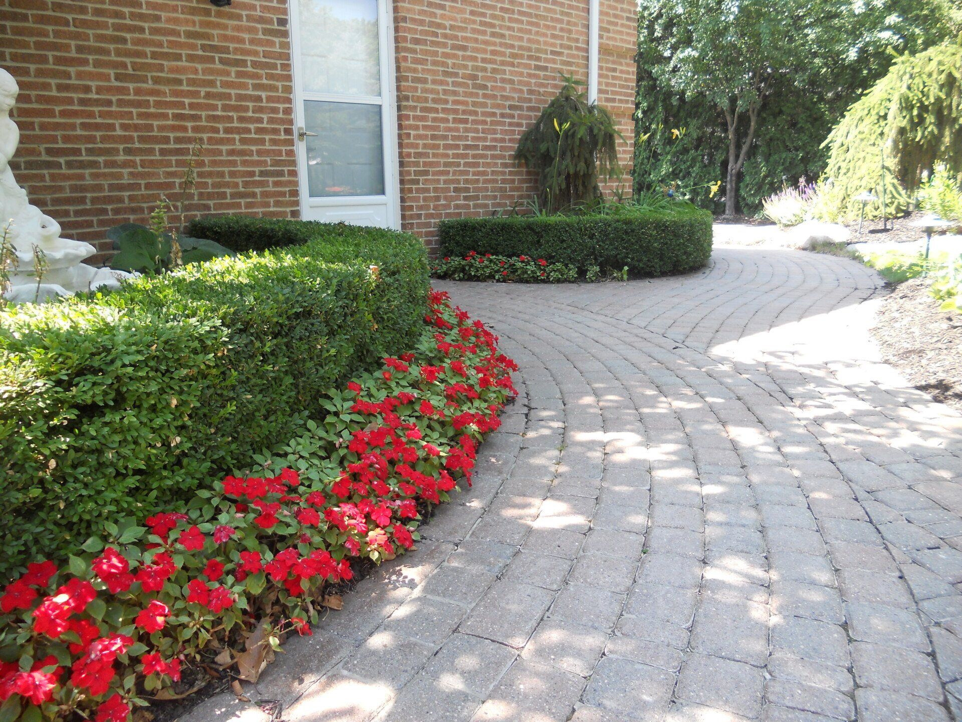 A brick walkway with red flowers on the side of it