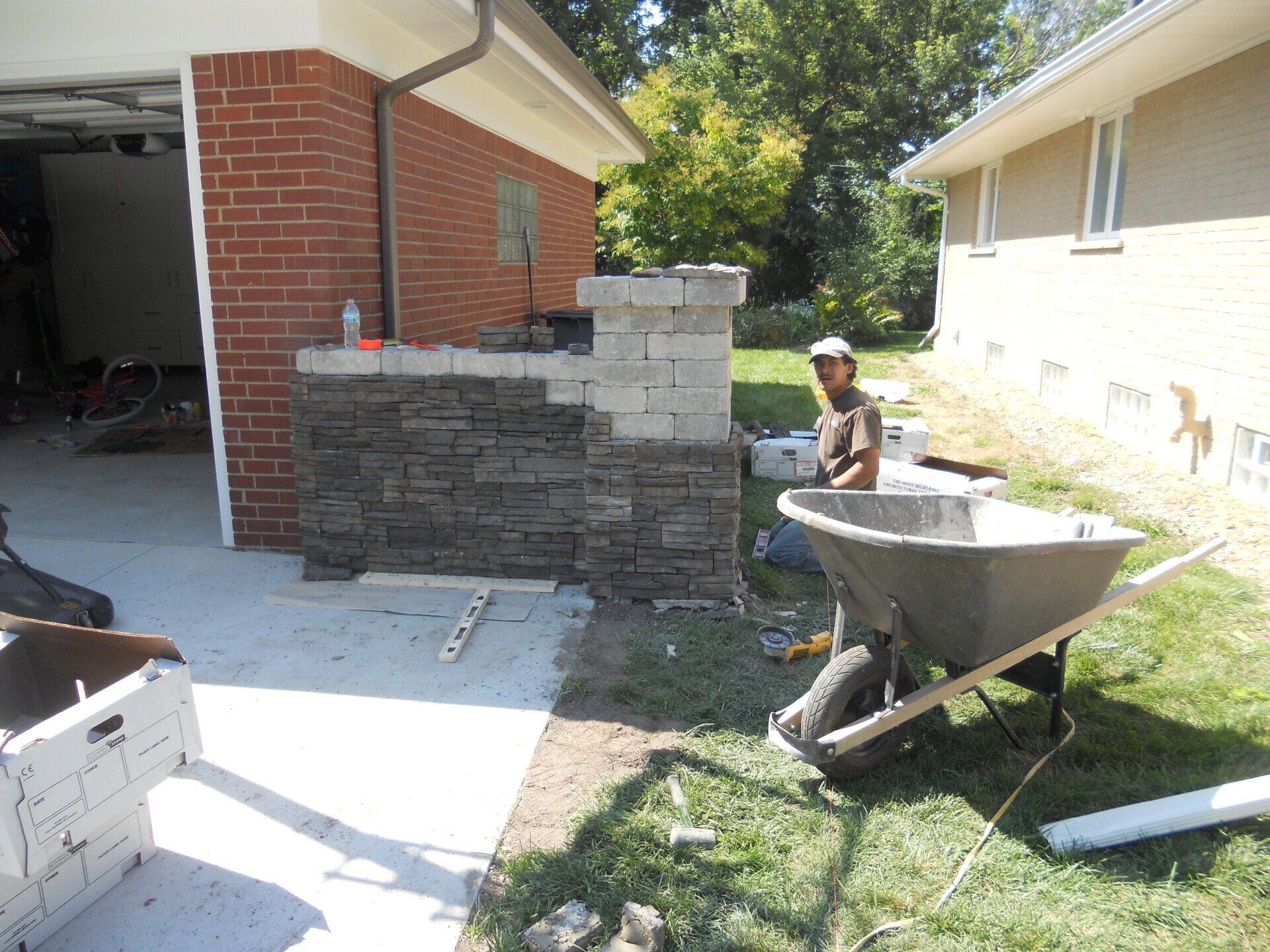 A man is sitting in a wheelbarrow in front of a brick house.