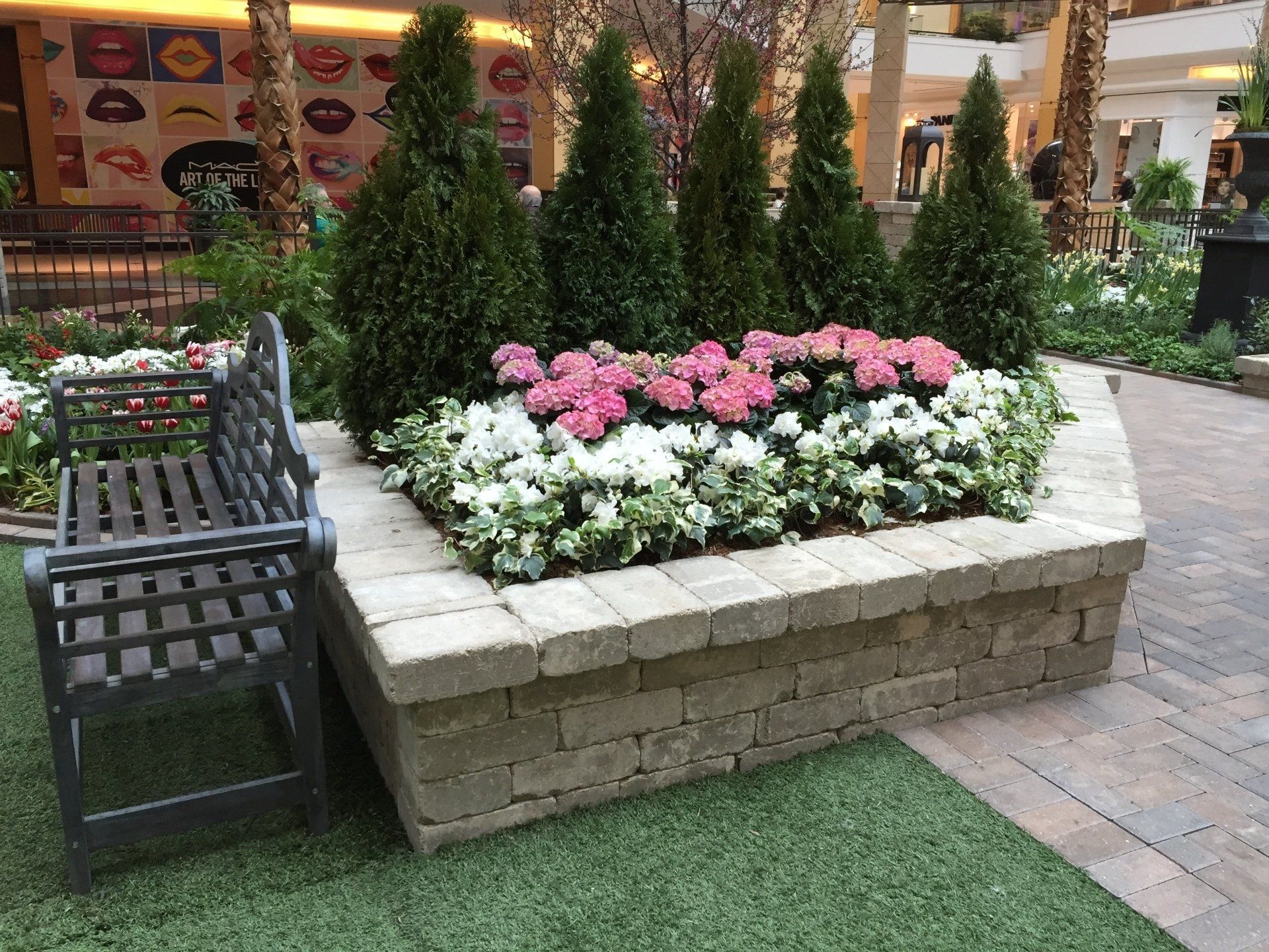 A bench is sitting next to a planter filled with pink and white flowers.
