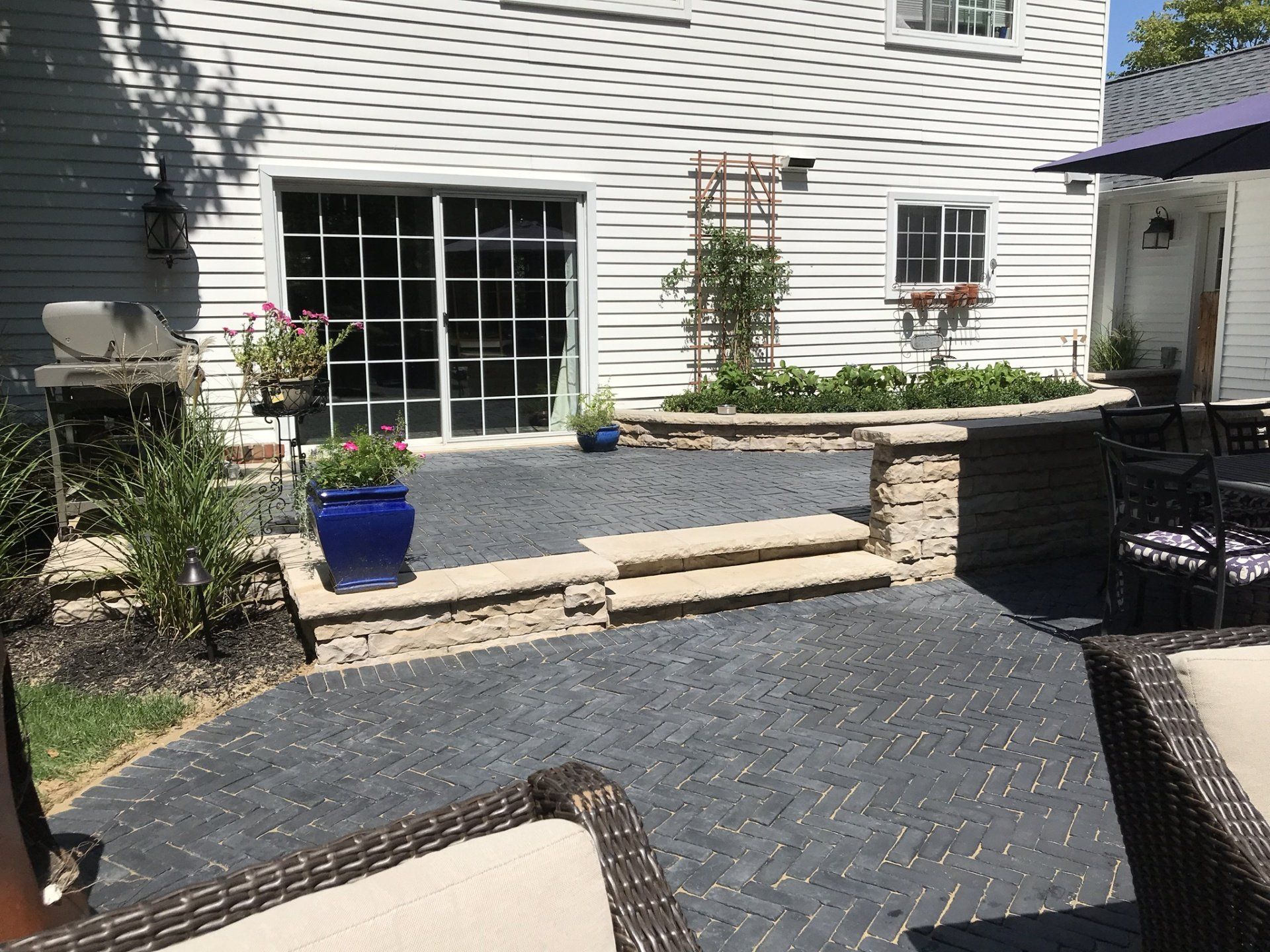 A patio with chairs and umbrellas in front of a white house.