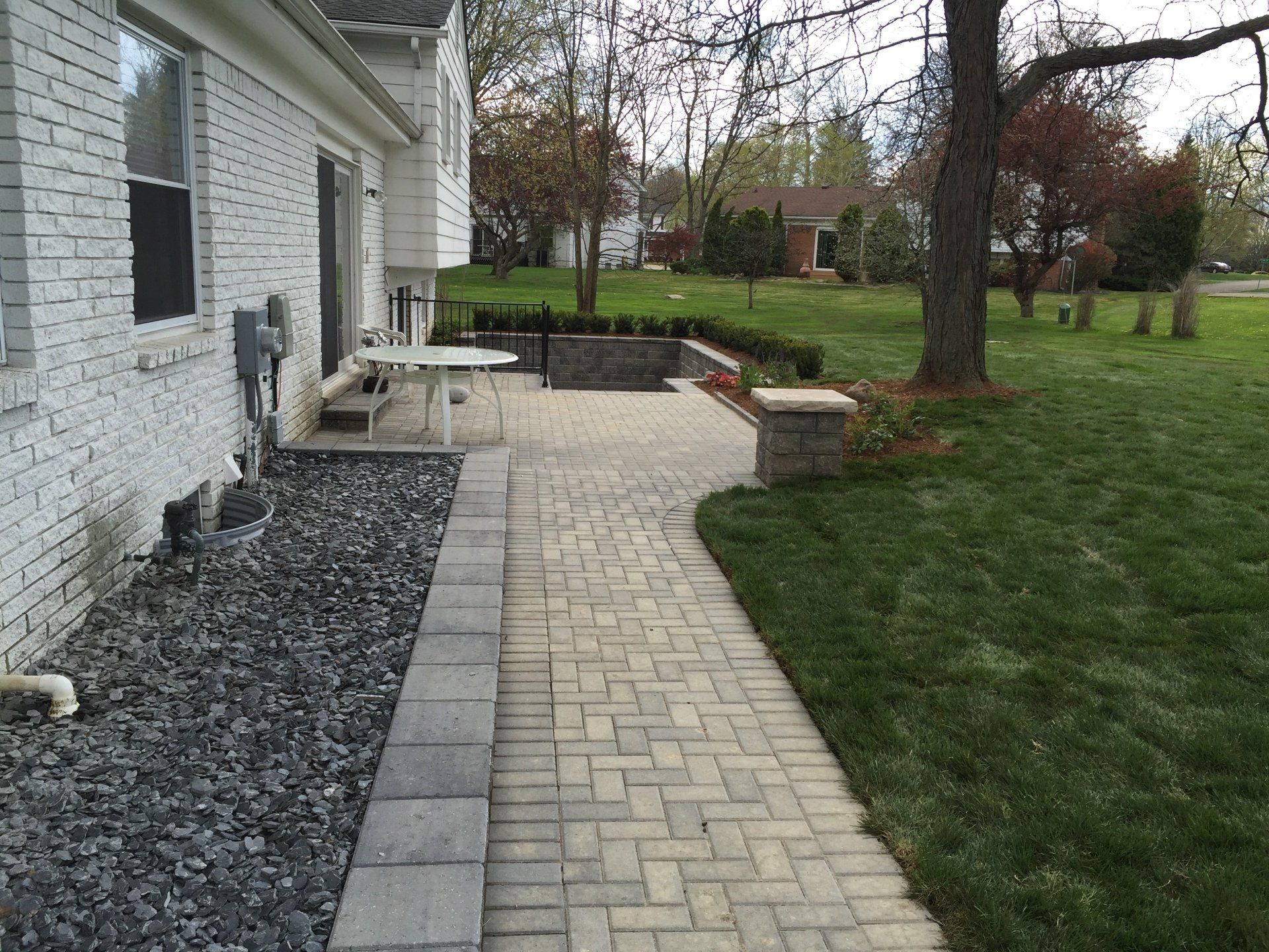 A brick walkway leading to a patio in front of a white brick house