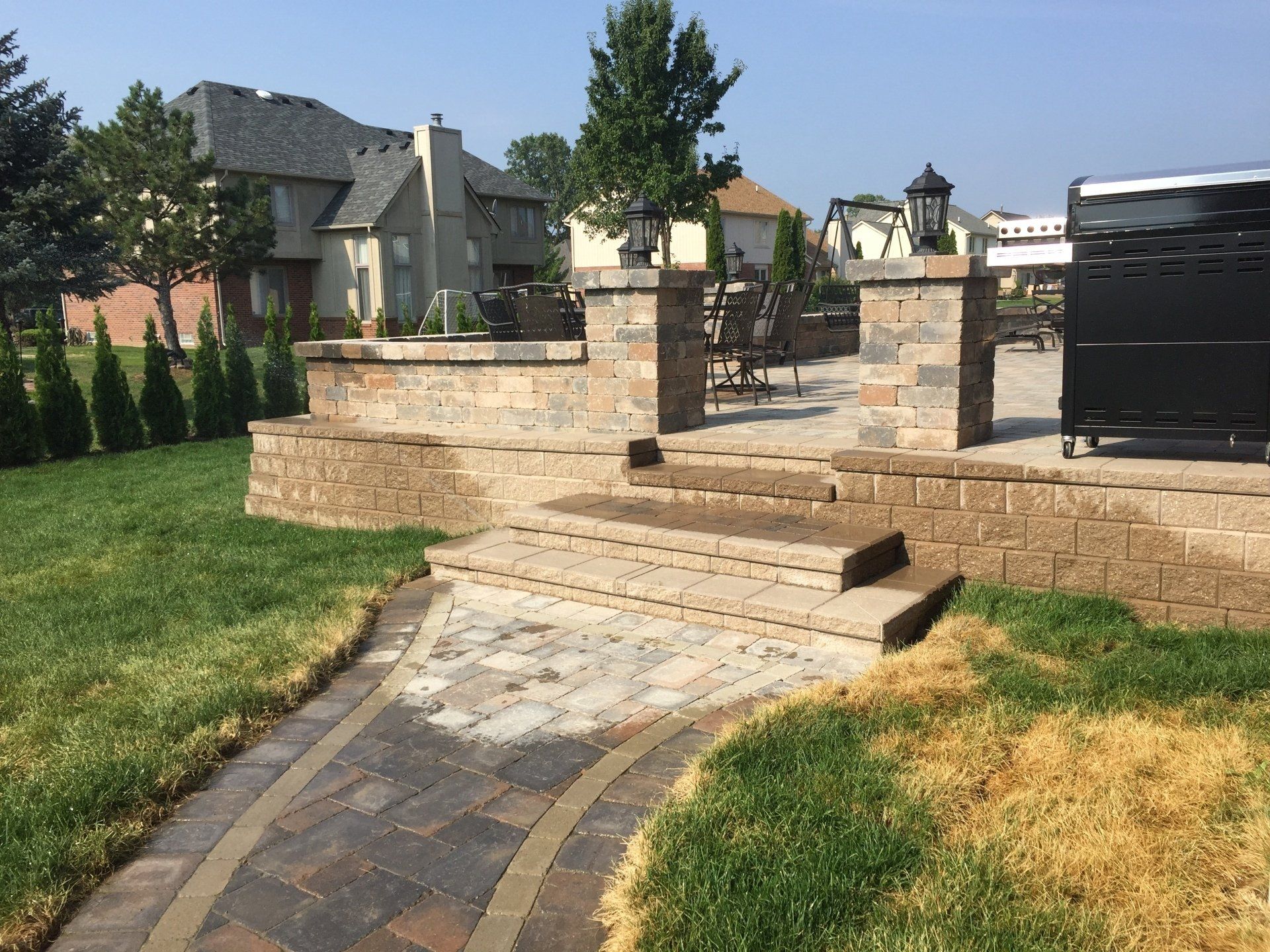 A brick walkway leading to a patio in a backyard