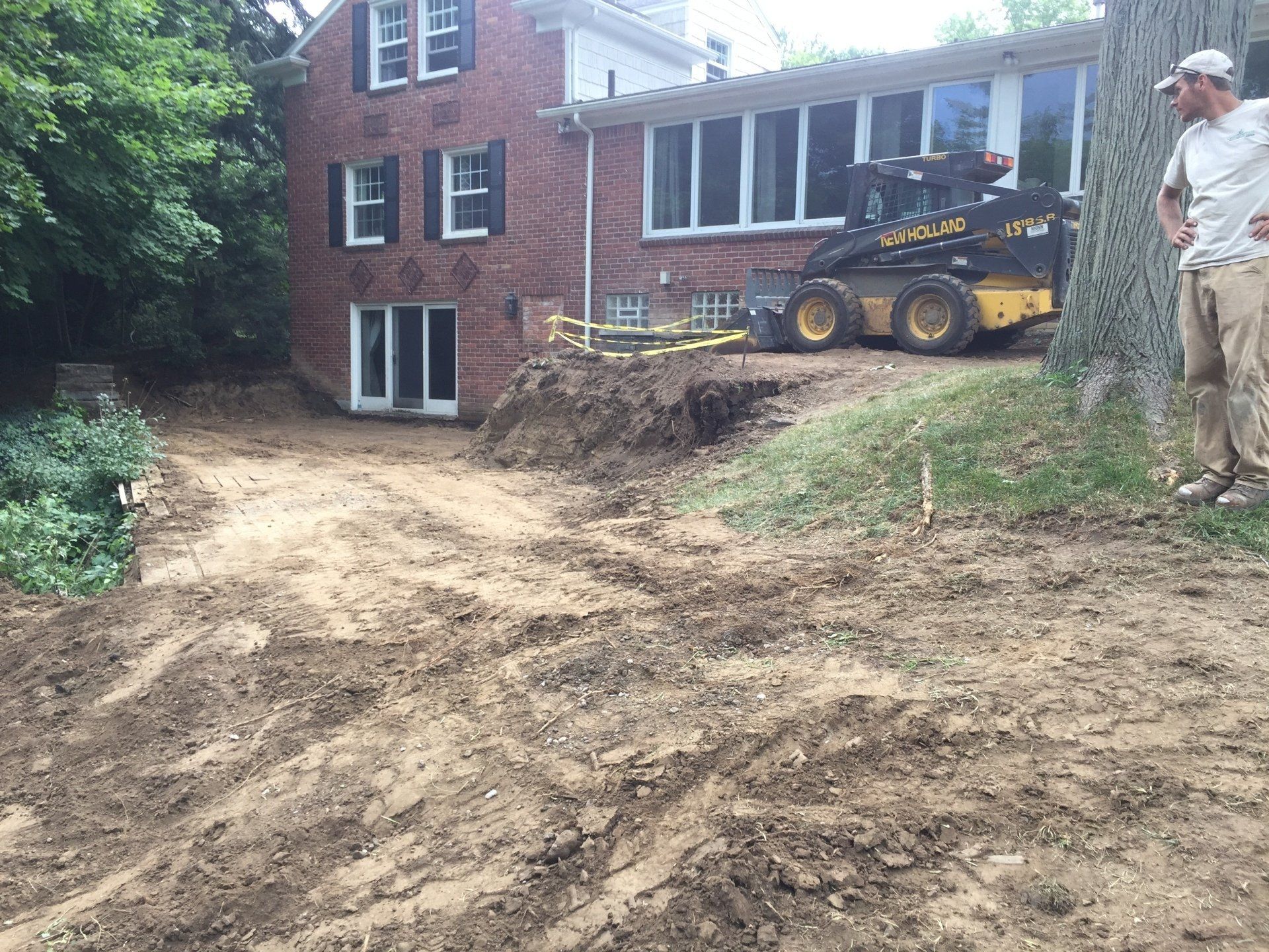 A man is standing in front of a house with a bulldozer parked in front of it.