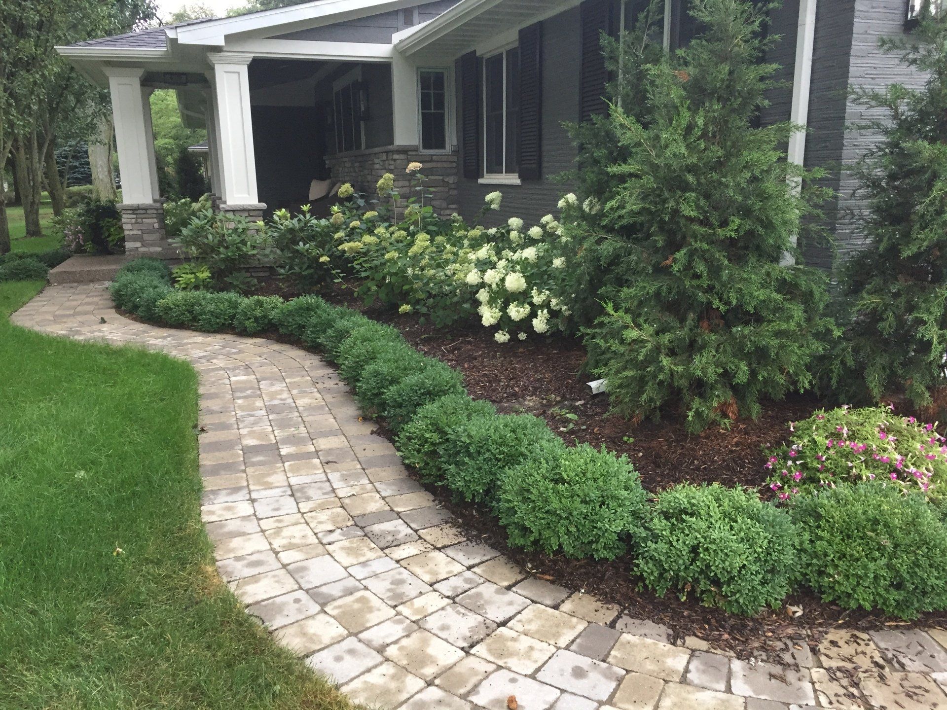 A brick walkway leading to a house with a lush green lawn.