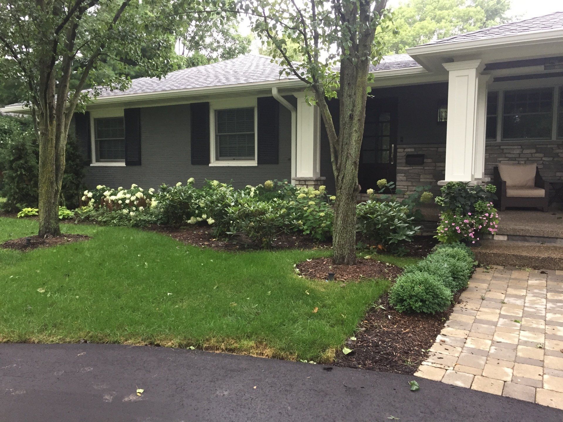 A house with black shutters and a brick driveway