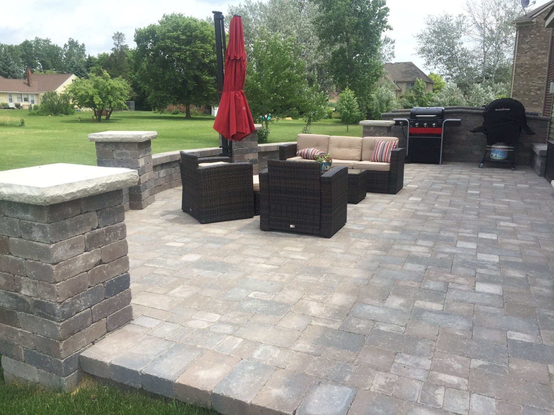 A patio with a couch and chairs and a red umbrella