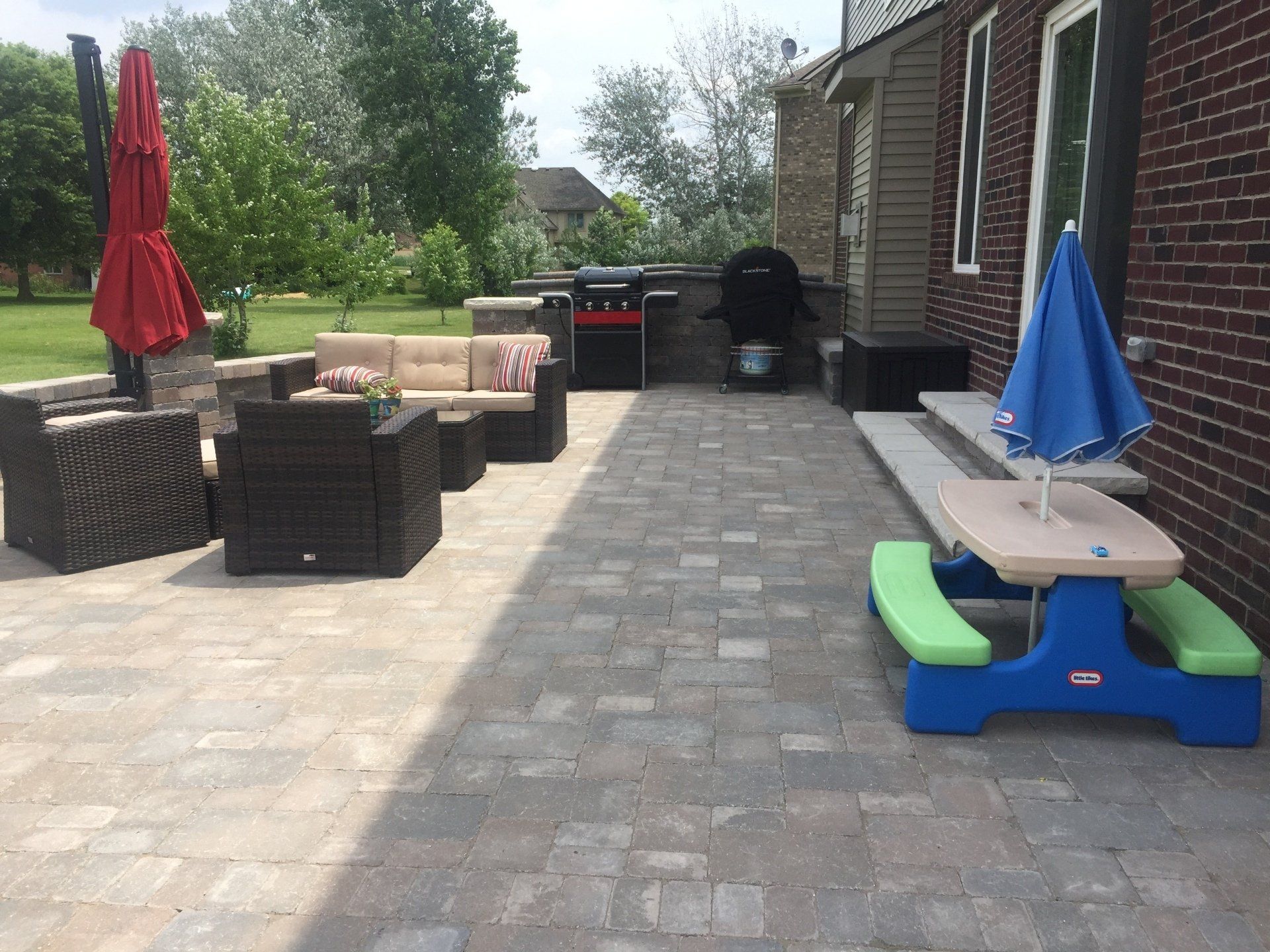 A patio with a picnic table , chairs , umbrellas and a grill.