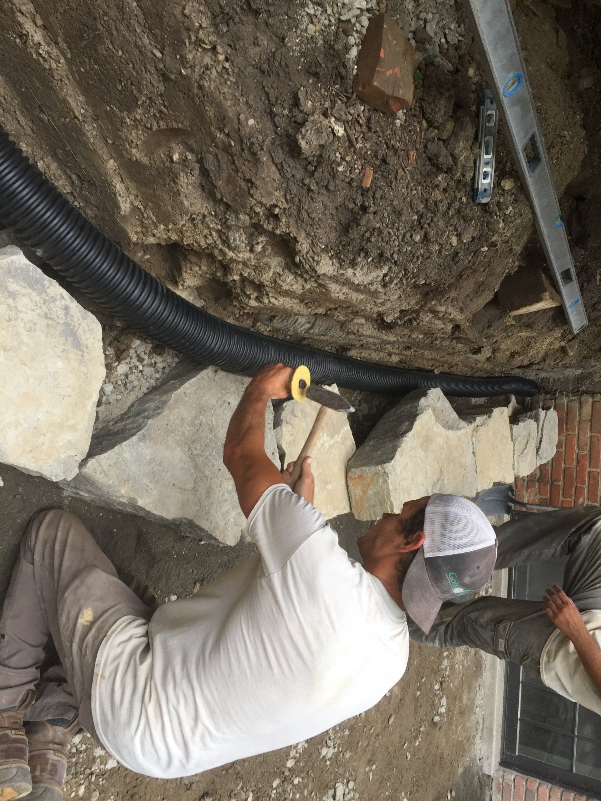 A man is kneeling down in the dirt holding a tape measure.