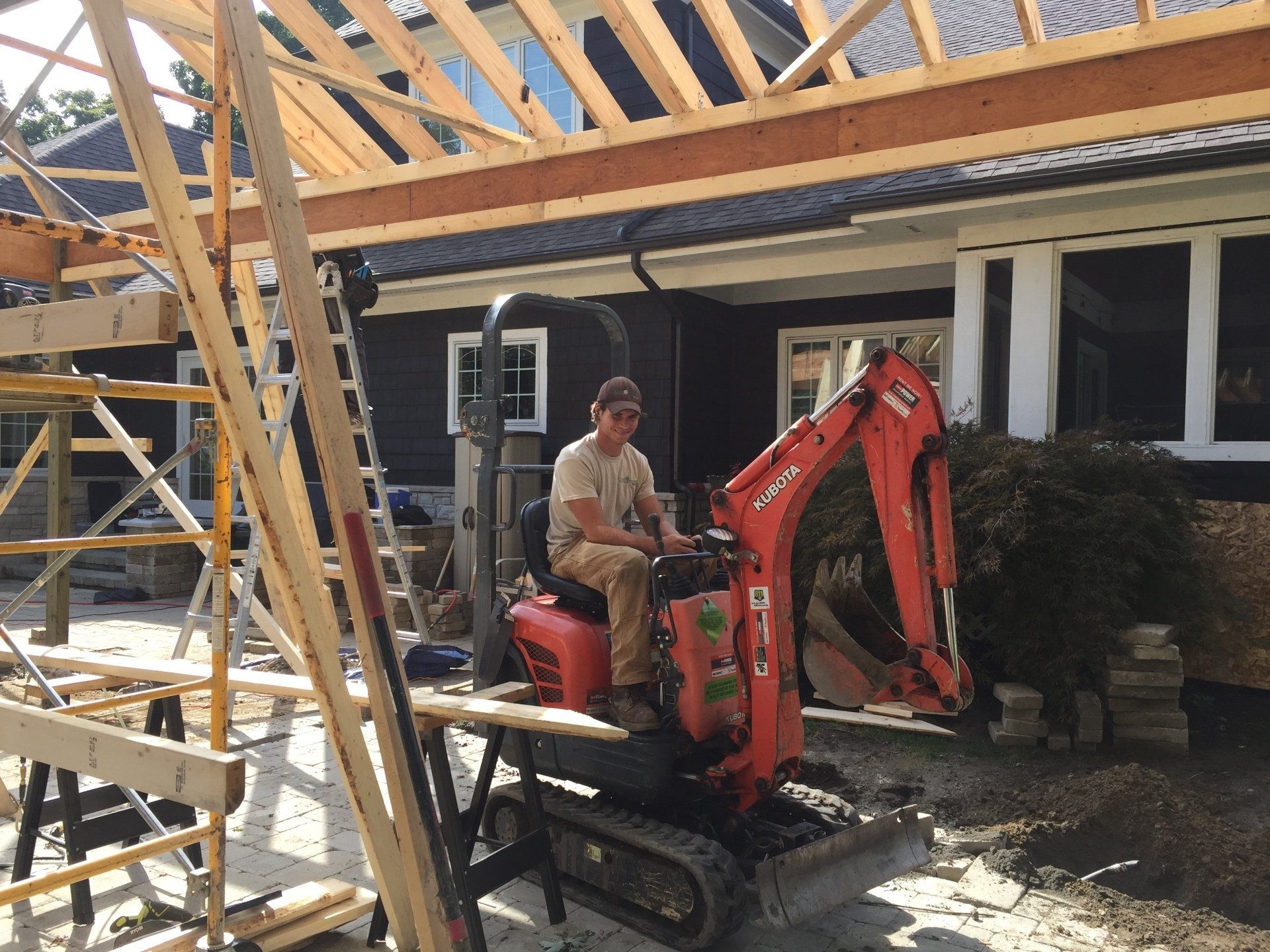 A man is sitting on a small excavator in front of a house under construction.