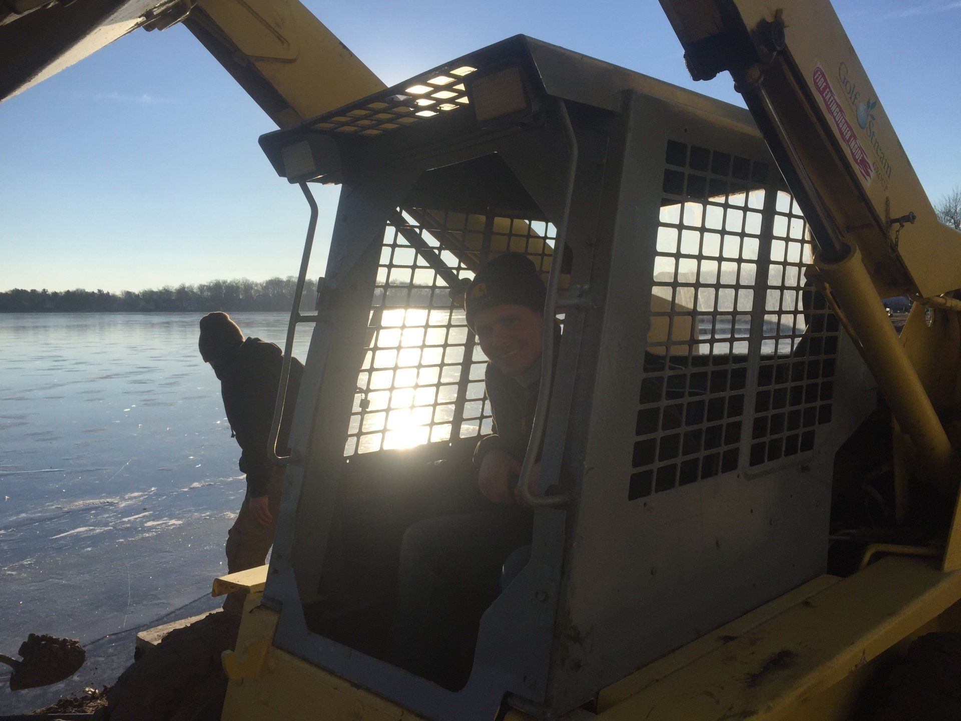 A man sits in the driver 's seat of a bulldozer near a body of water