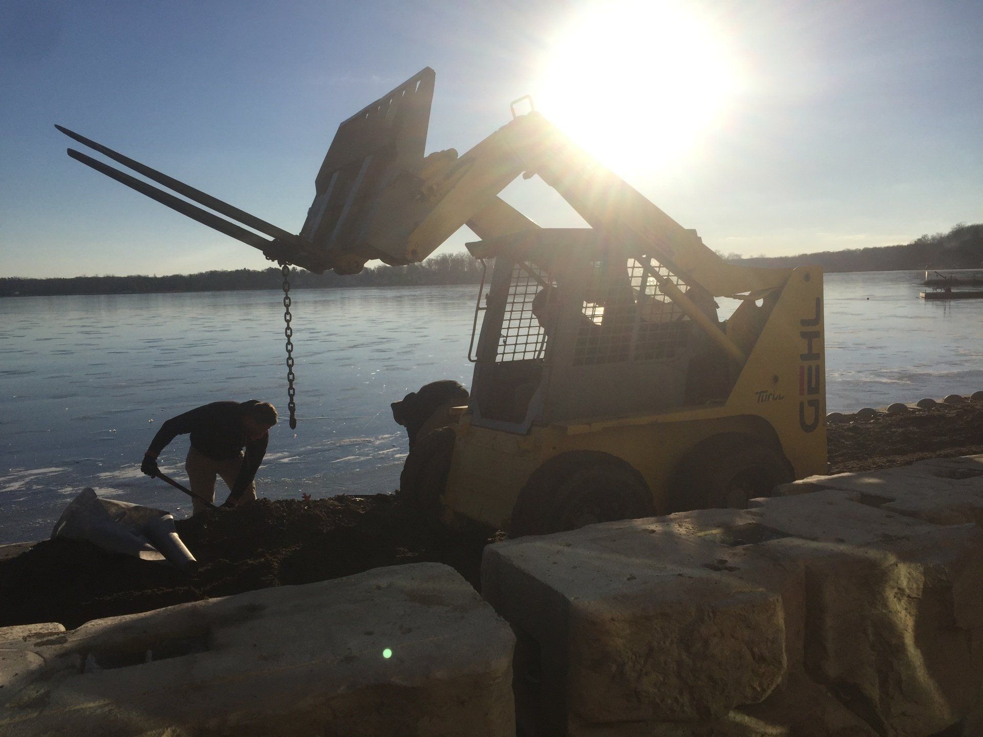 A yellow bulldozer is parked on the shore of a lake