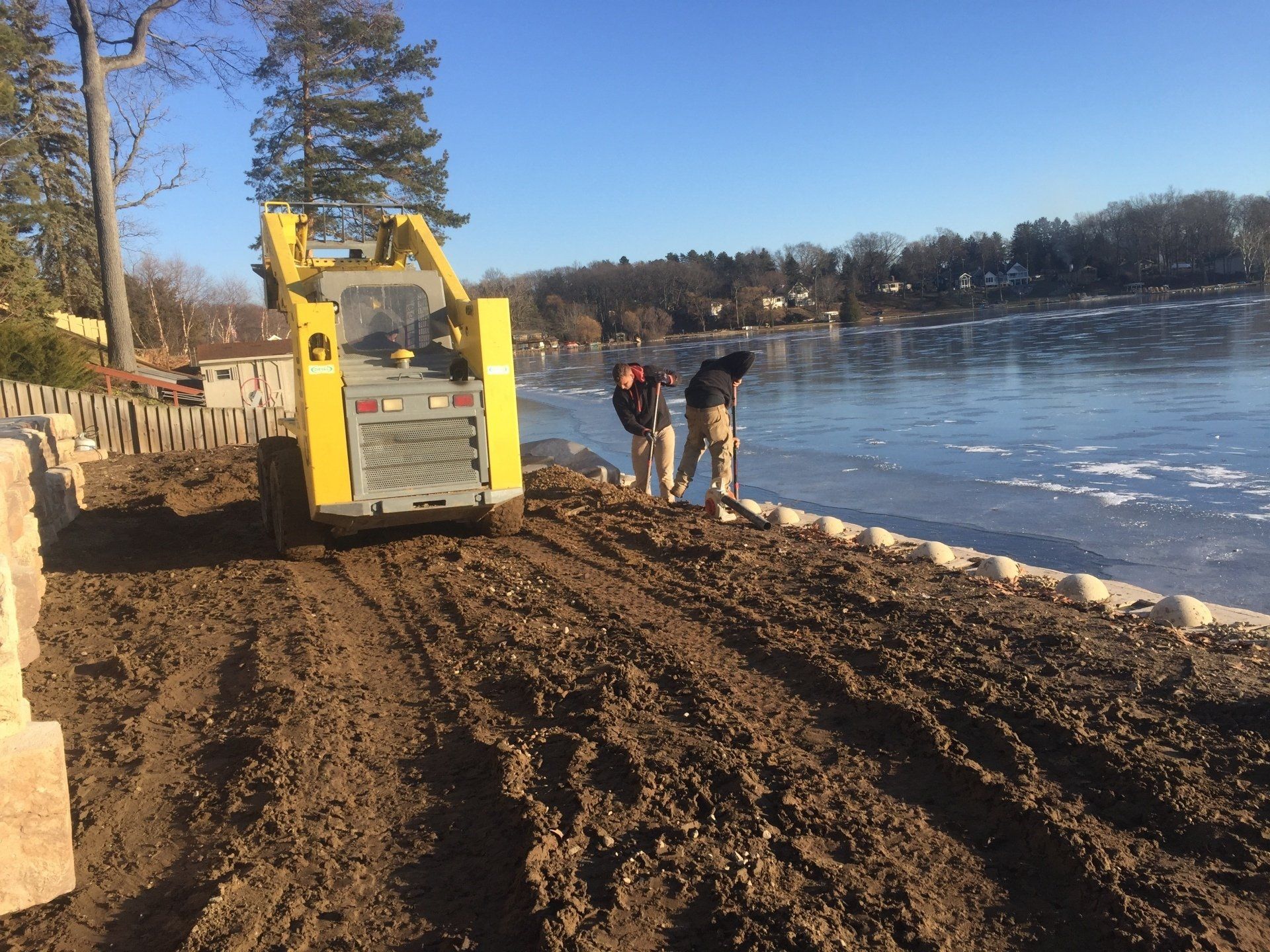 A man is standing next to a yellow bulldozer on a dirt road near a lake.