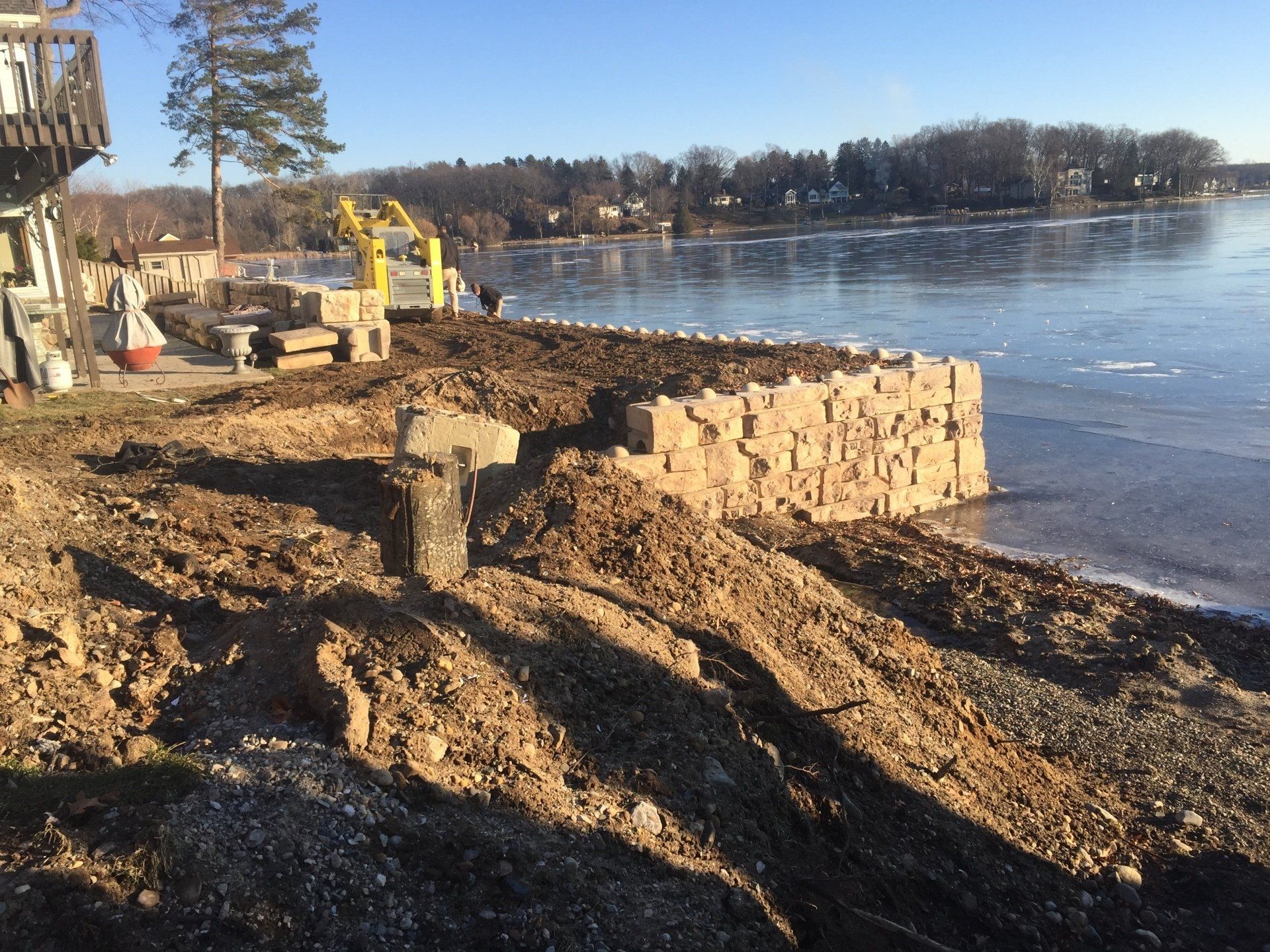 A yellow excavator is on the shore of a lake