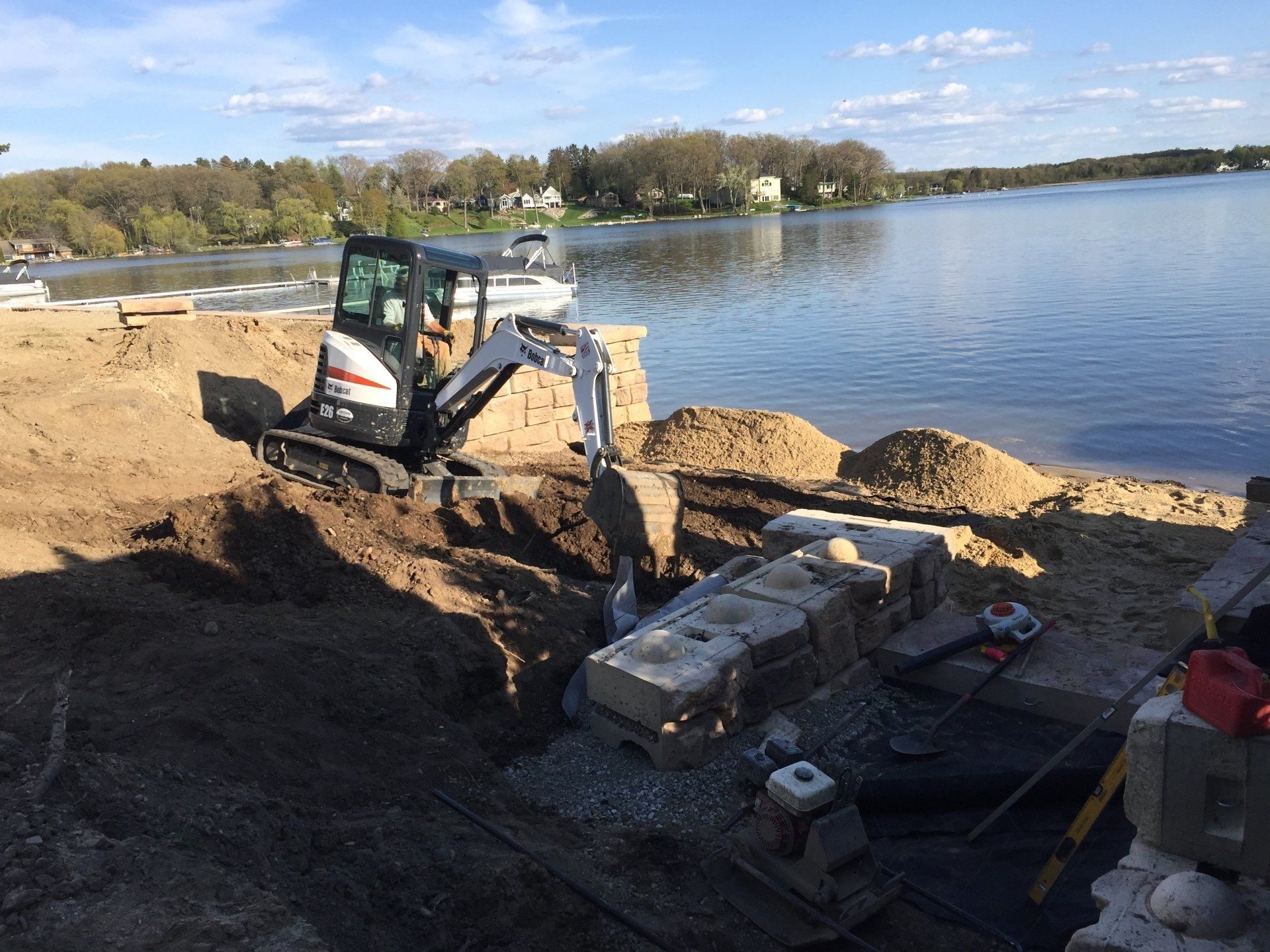 A small excavator is digging a hole on the shore of a lake.