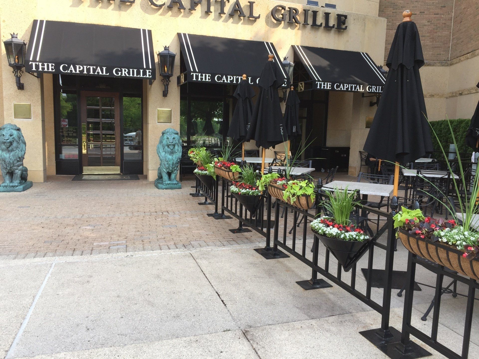 A restaurant called the capital grille has tables and umbrellas outside