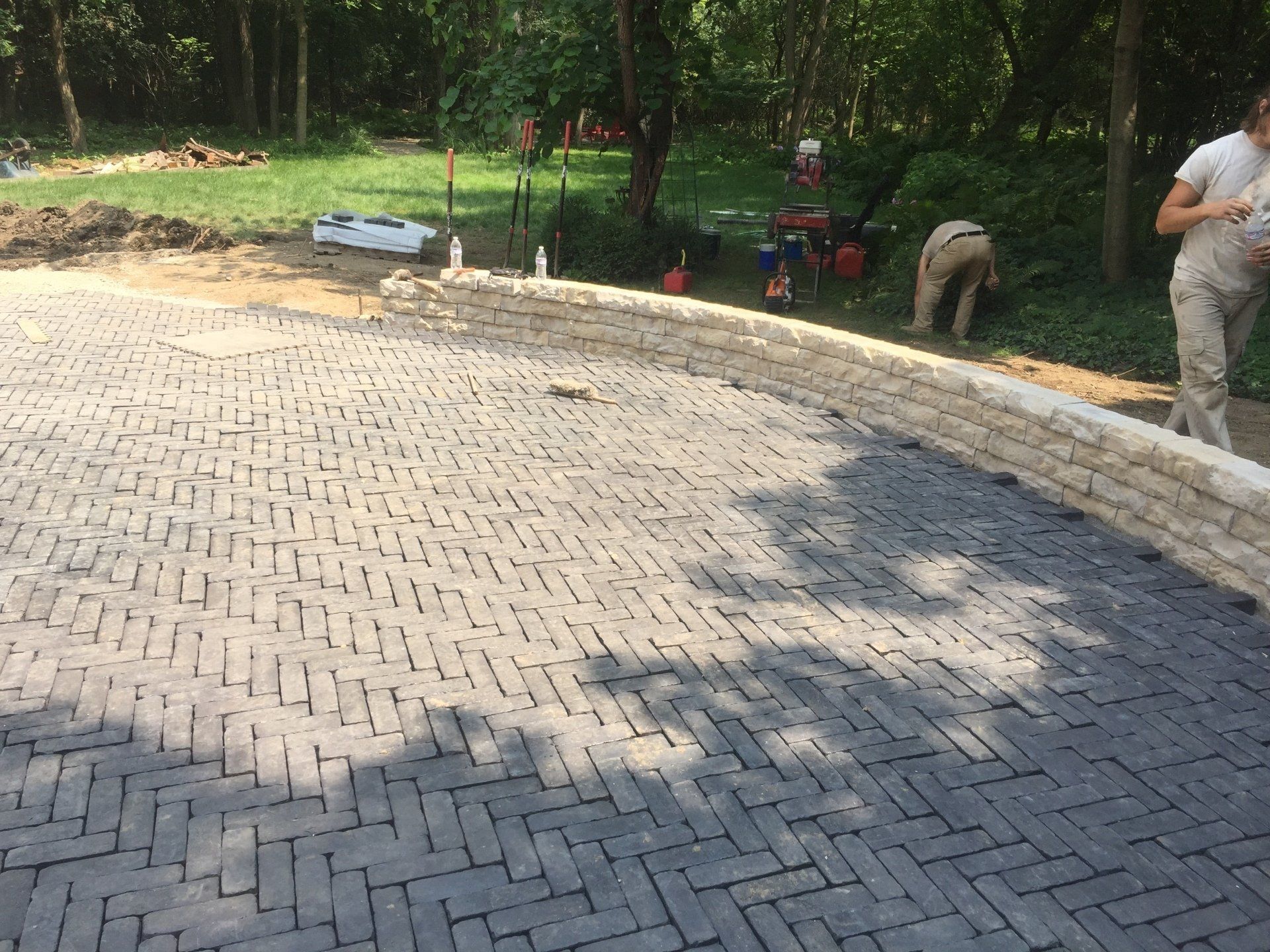 A woman is standing on a brick driveway next to a wall.