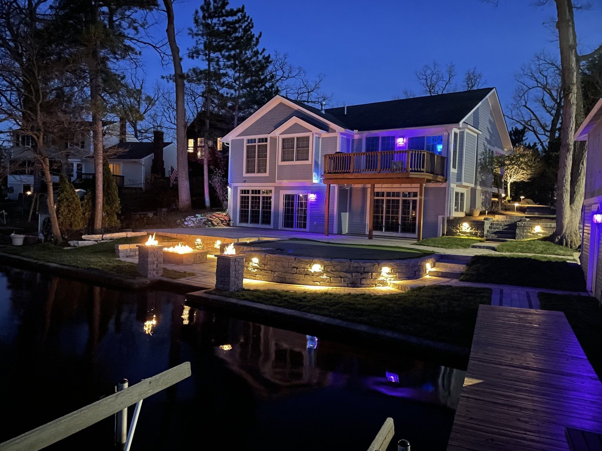 A large house is lit up at night next to a body of water.