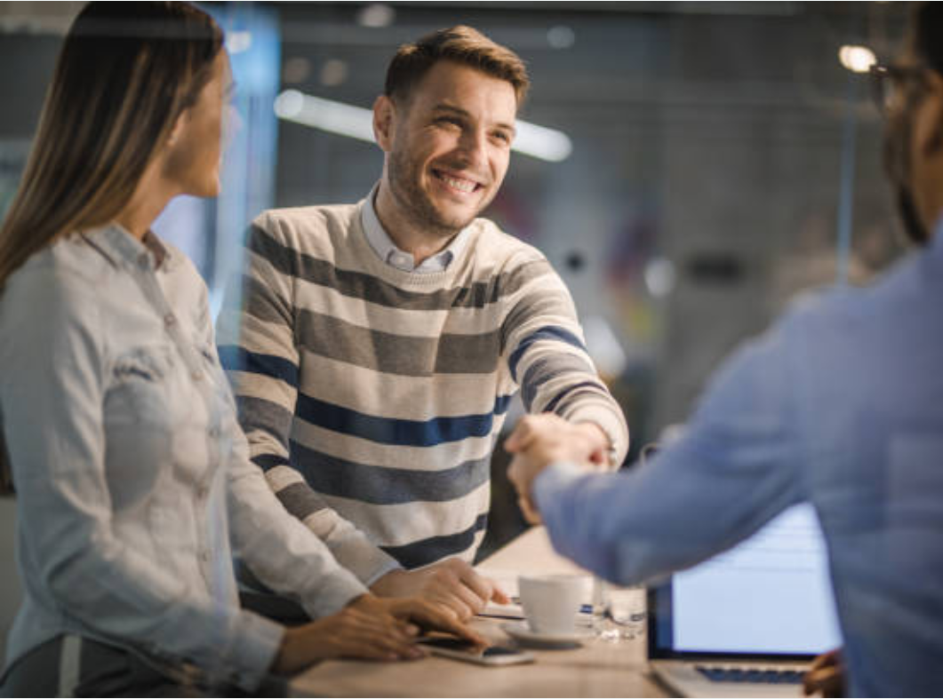 A man and a woman are shaking hands with a man in an office.