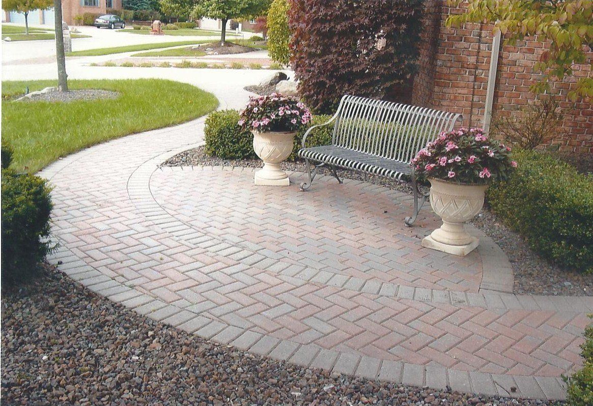 A brick walkway with a bench and vases of flowers