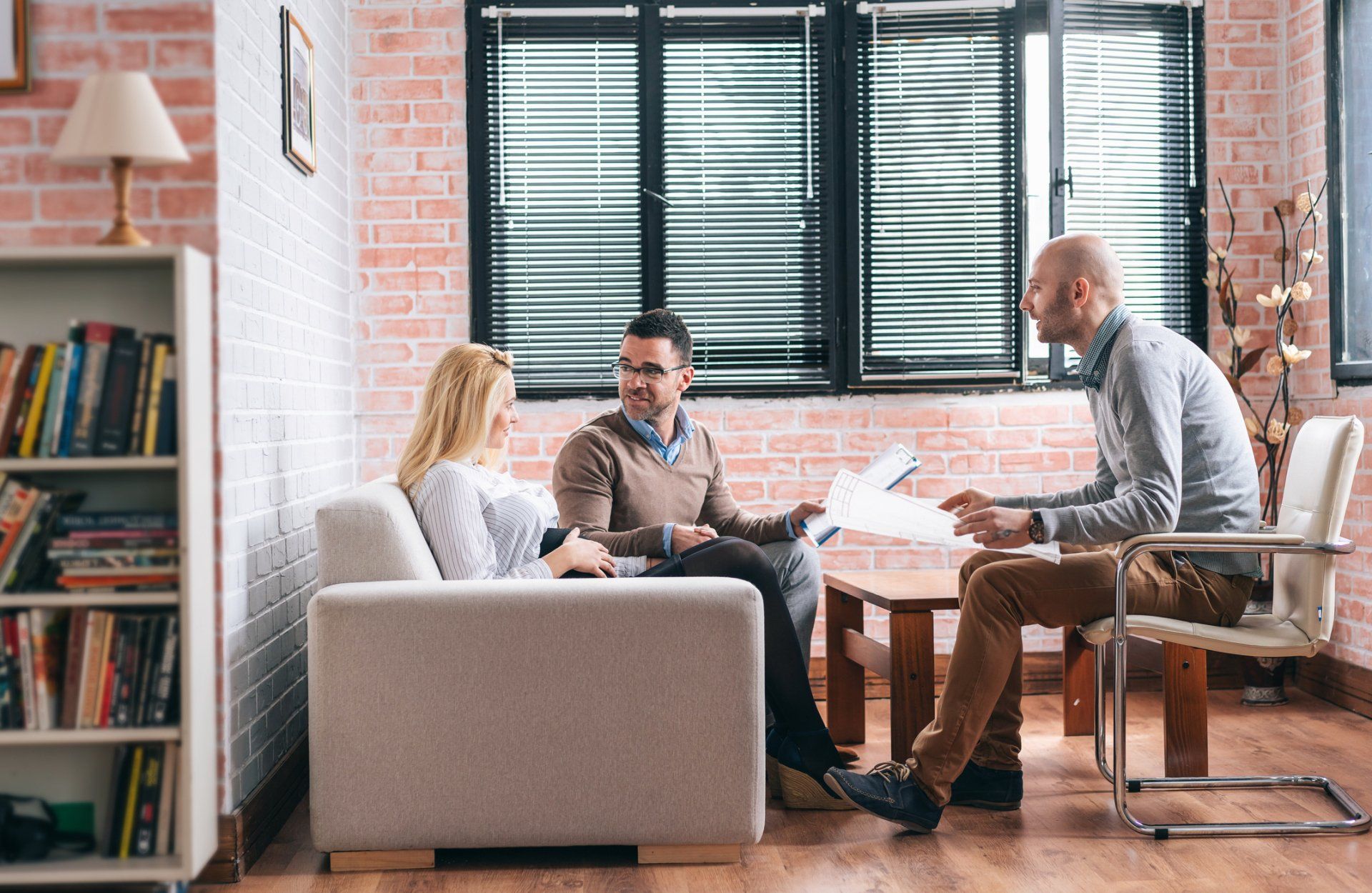 A group of people are sitting on a couch in a living room talking to each other.
