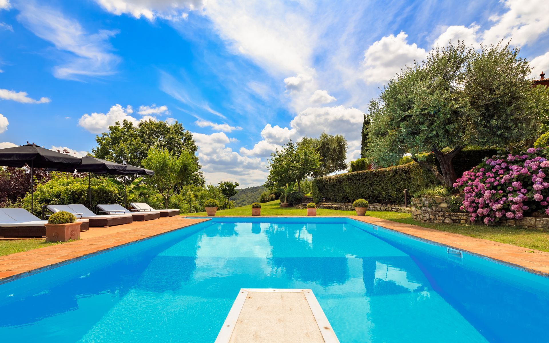A large swimming pool surrounded by lawn chairs and umbrellas on a sunny day.