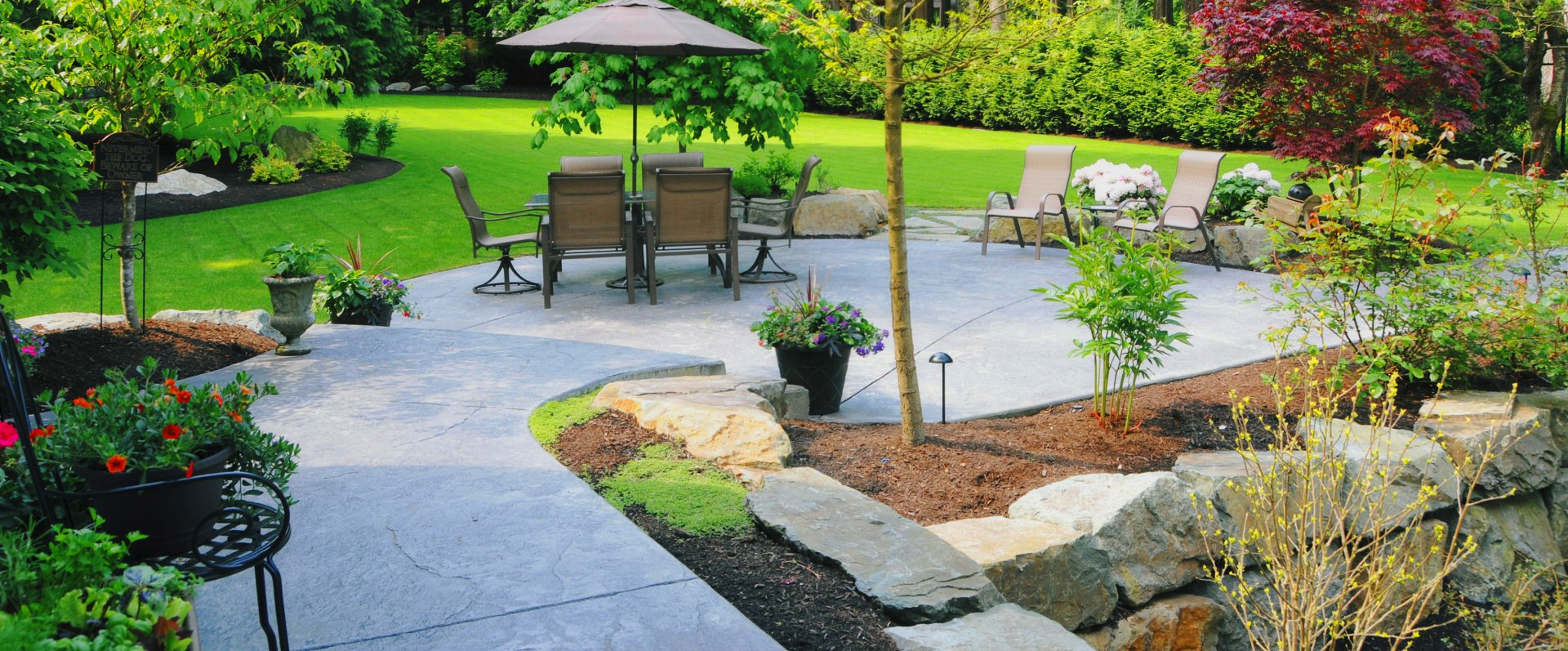 There is a patio with a table and chairs and an umbrella in the backyard.