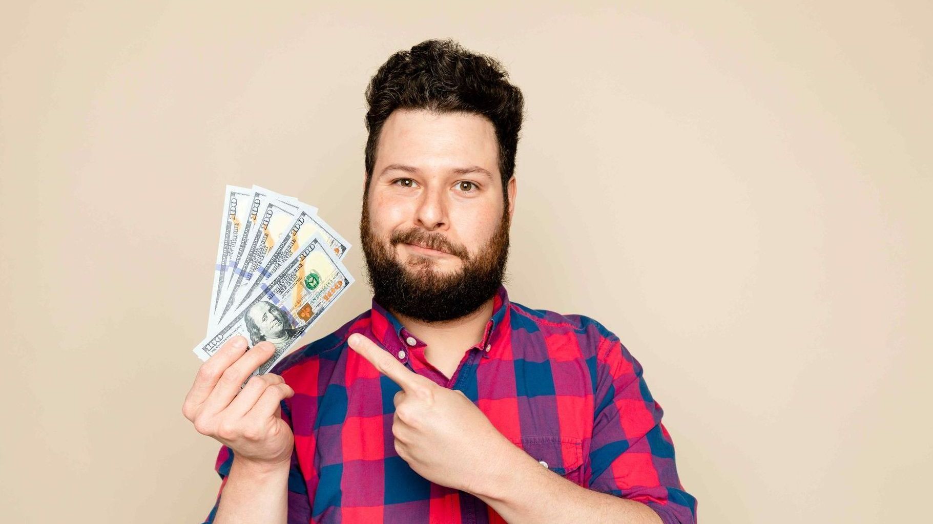 man pointing with his left hand to the money he is holding in his right hand while smirking