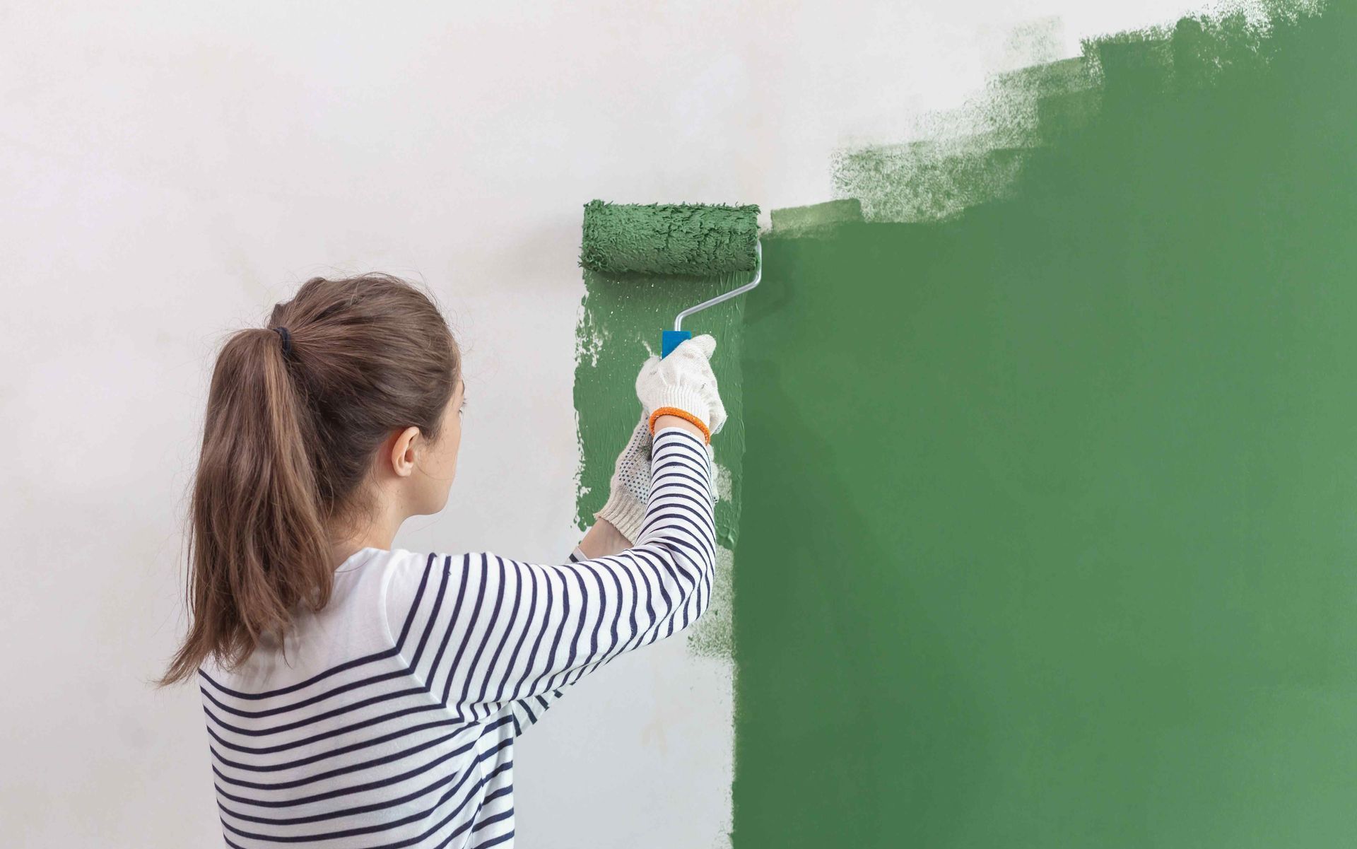 woman painting the wall green with roller