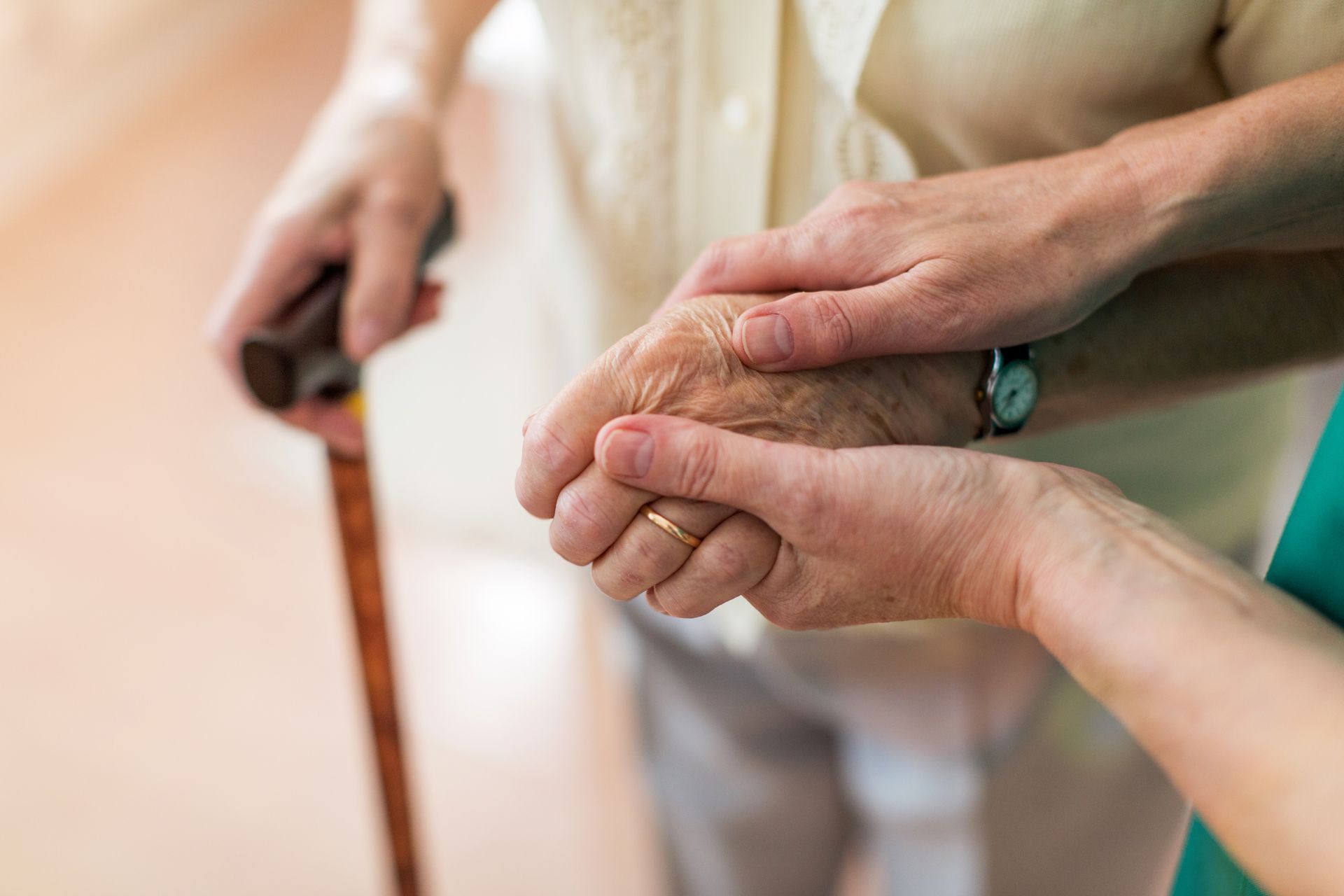 Hands clasped, one older person using a cane, being assisted by another, wearing a light green shirt