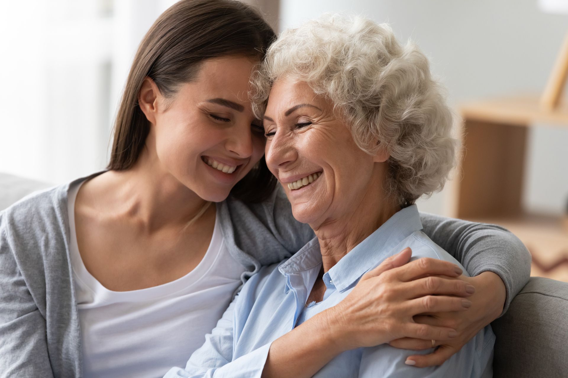 Young woman embraces and smiles with an older woman, indoors. Both are smiling