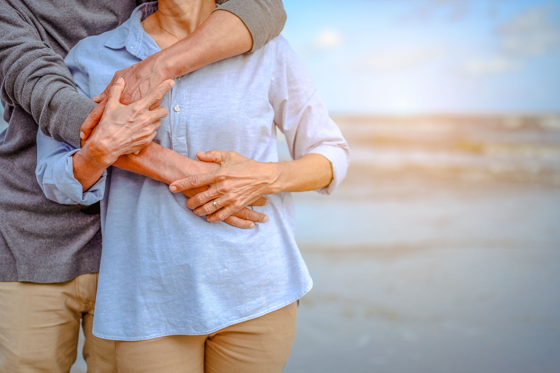 Elderly couple embracing on a beach, sunlight in the background