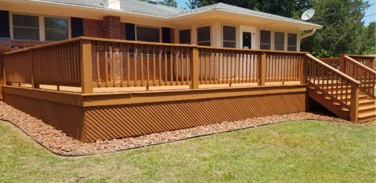 A large wooden deck with stairs is in front of a house.