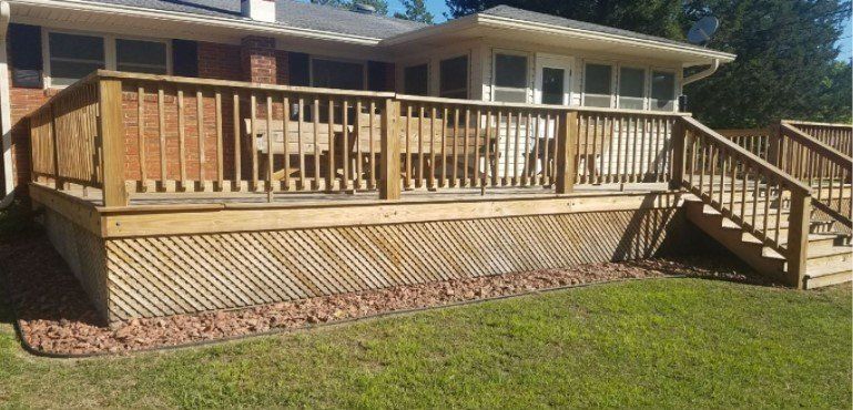 A large wooden deck with stairs leading up to it is in front of a house.