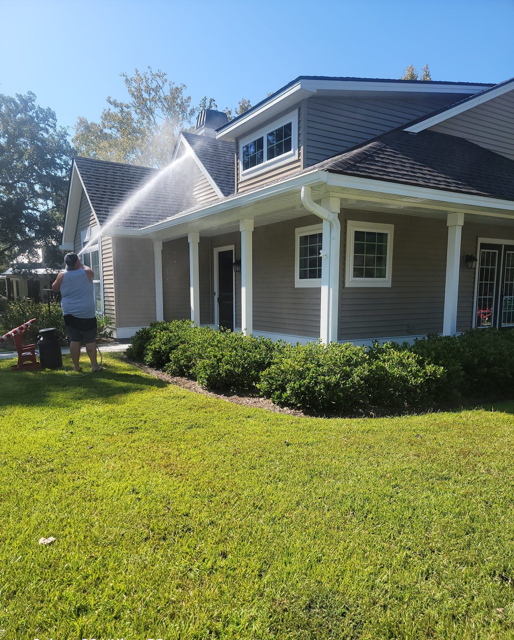 A man is cleaning the roof of a house with a pressure washer.