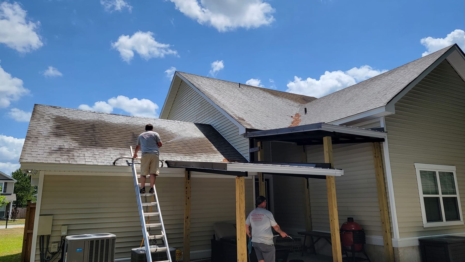 A man is standing on a ladder on the roof of a house.