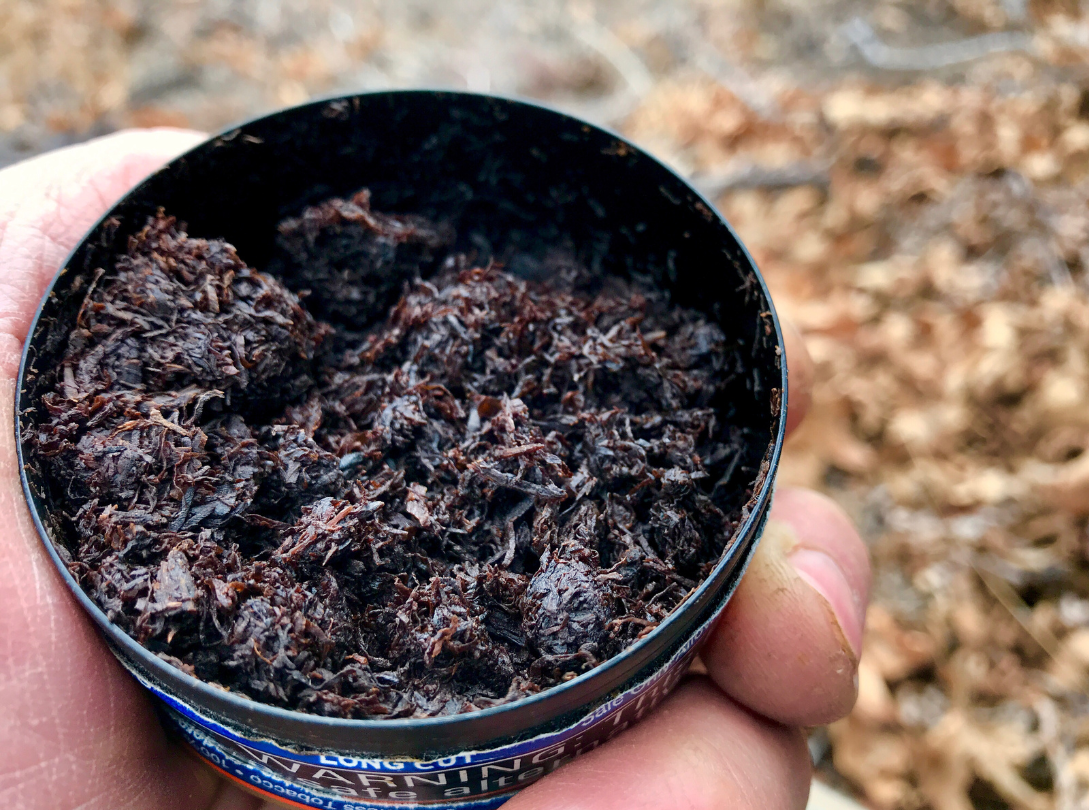 A person is holding a can of tobacco in their hand.