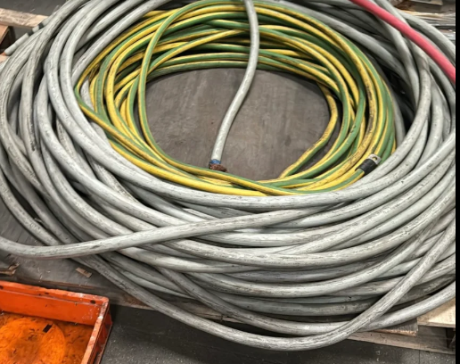 Cavo elettrico grigio arrotolato con un tubo flessibile giallo e verde all'interno, su una superficie di legno.