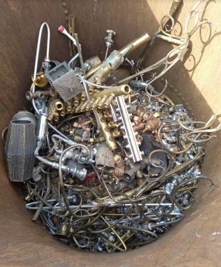 Mucchio di rottami metallici in un contenitore metallico, tra cui fili, tubi e parti meccaniche assortite.