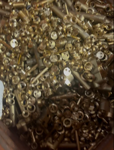 Un mucchio di piccole parti di macchinari lucide, color ottone o oro, probabilmente rottami metallici, in un contenitore.