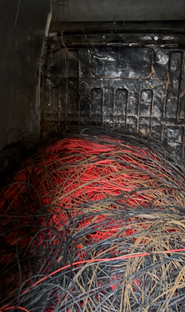 Un ammasso aggrovigliato di fili elettrici rossi e neri all'interno di un recinto buio.