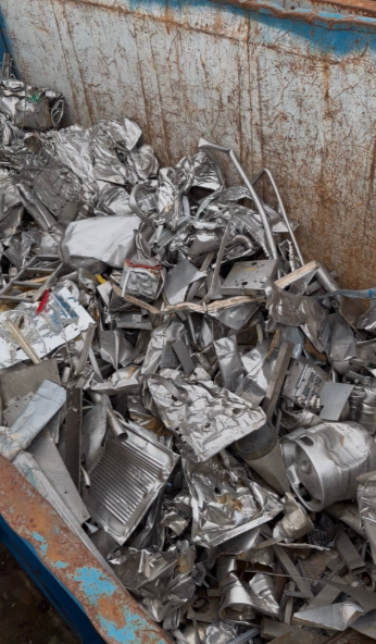 Mucchio di rottami metallici in un contenitore metallico, tra cui fili, tubi e parti meccaniche assortite.