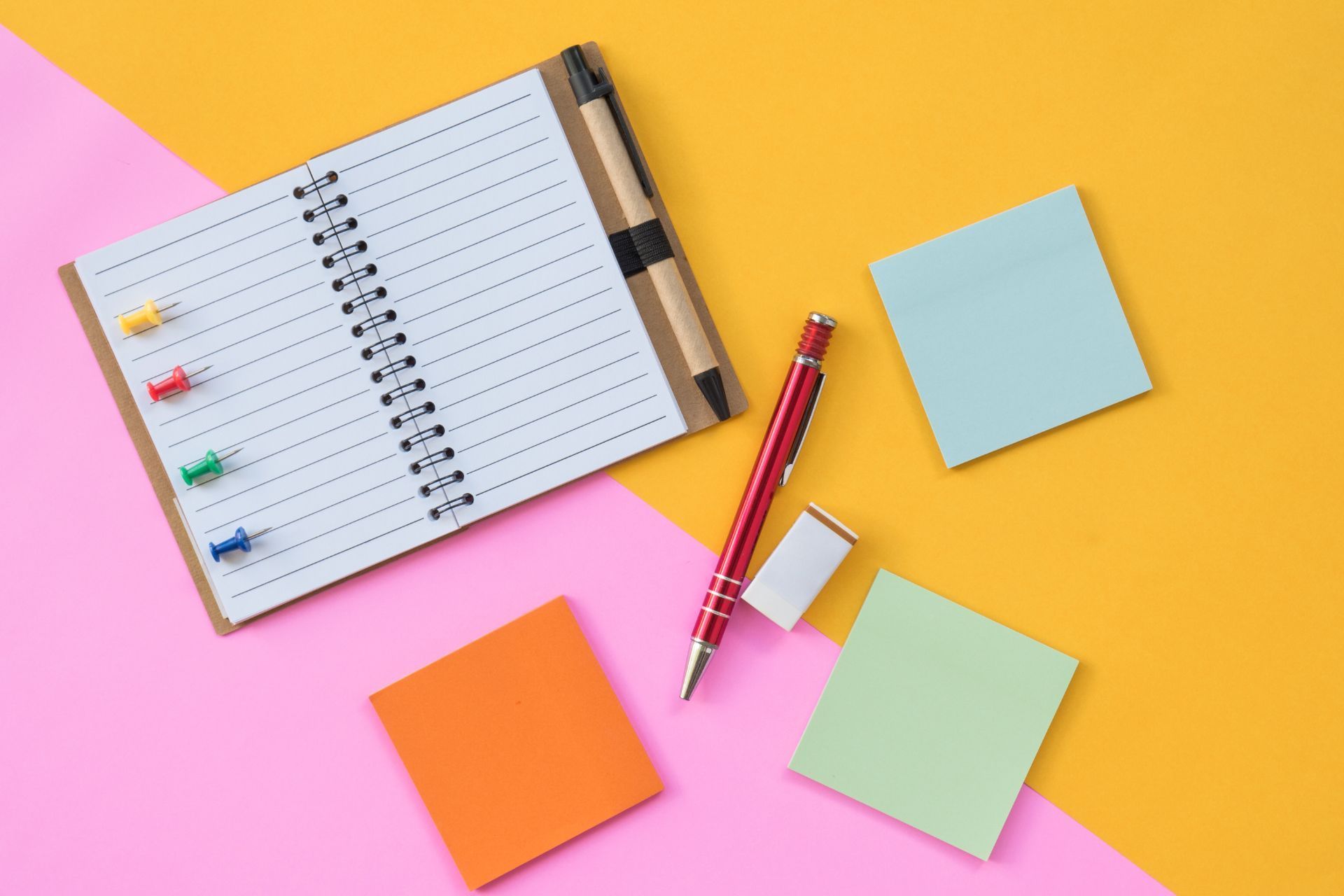 A notebook with sticky notes and a pen on a pink and yellow background.