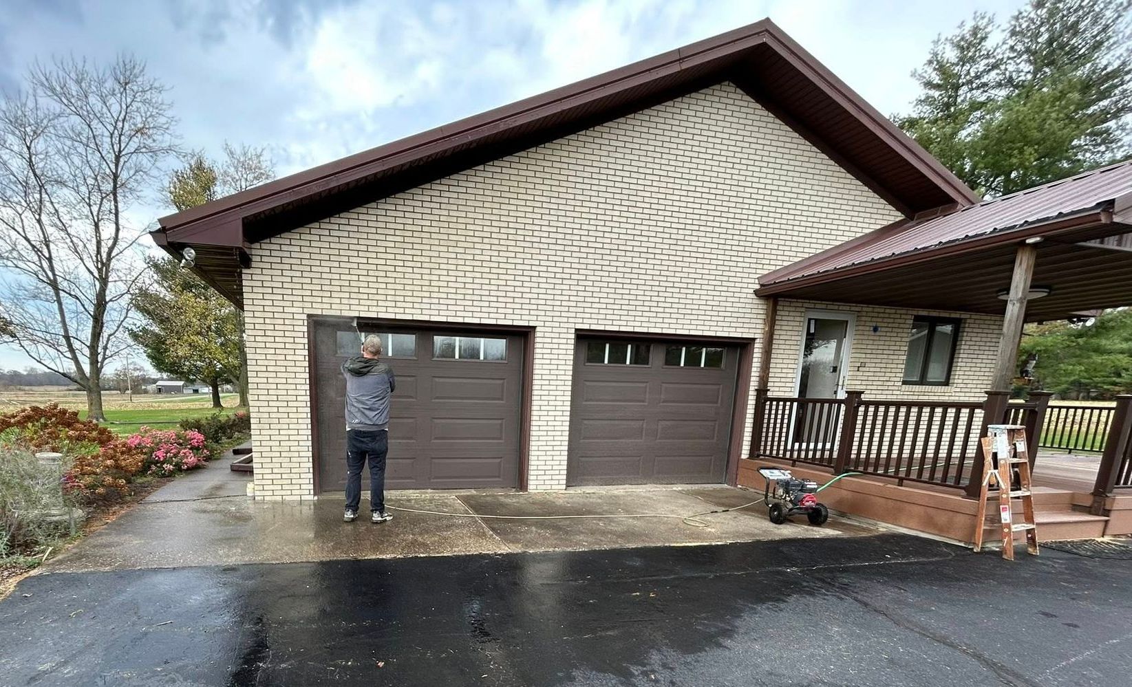 A person is using a high pressure washer to clean the side of a house.