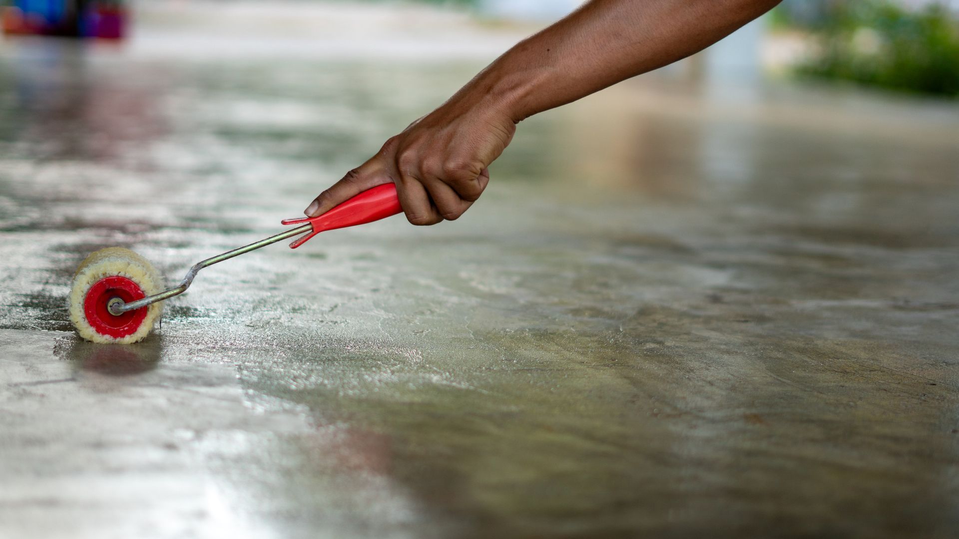 A person is painting a concrete floor with a paint roller.