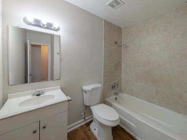 Bathroom with white vanity, toilet, and bathtub. Beige tiled wall and light brown floor.