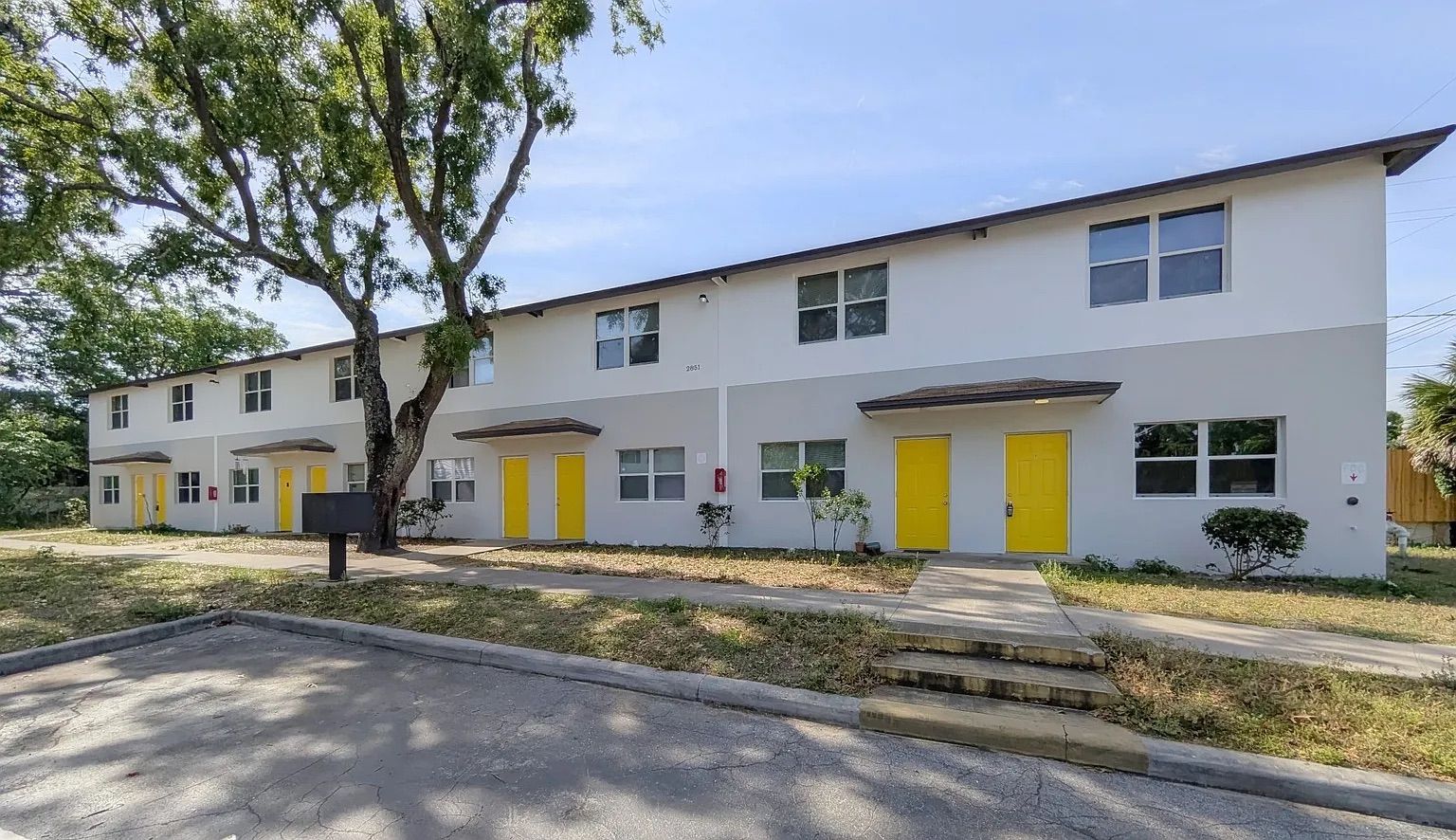 Row of two-story townhouses with gray and white exteriors, yellow doors, and small front porches.
